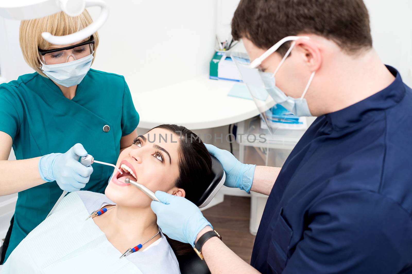 Male dentist treating patient teeth with assistant