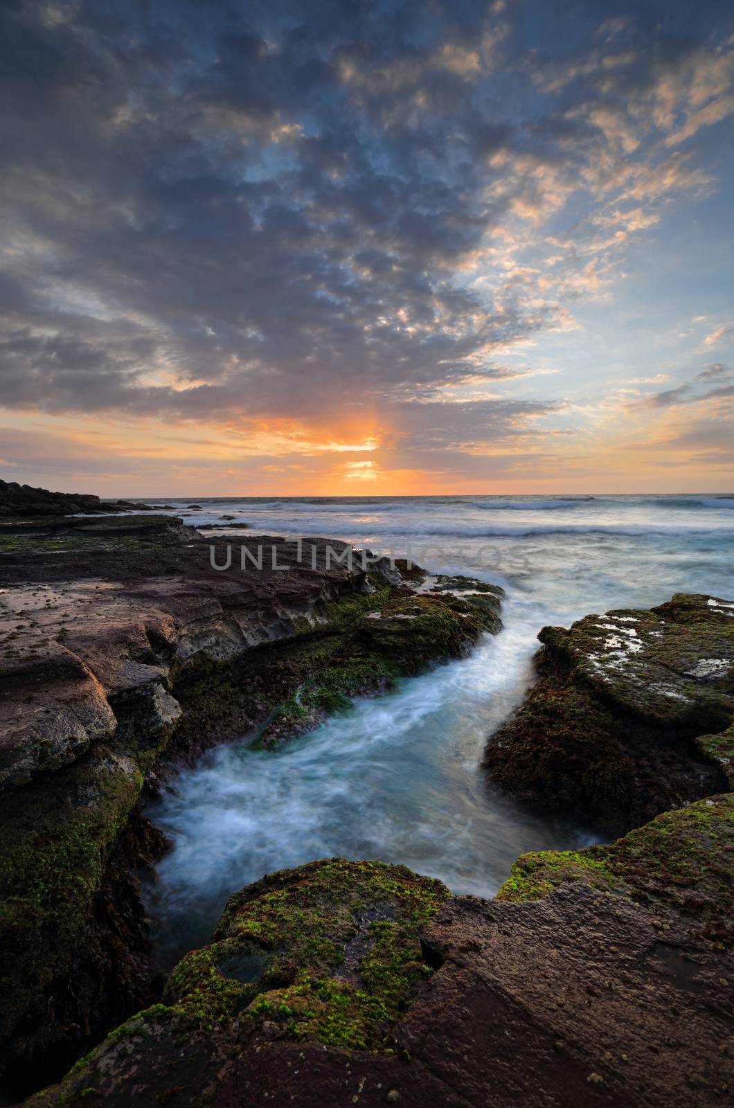 Beautiful coastal sunrise with tidal ocean flows into craggy eroded rock channel growing green and red moss or algae