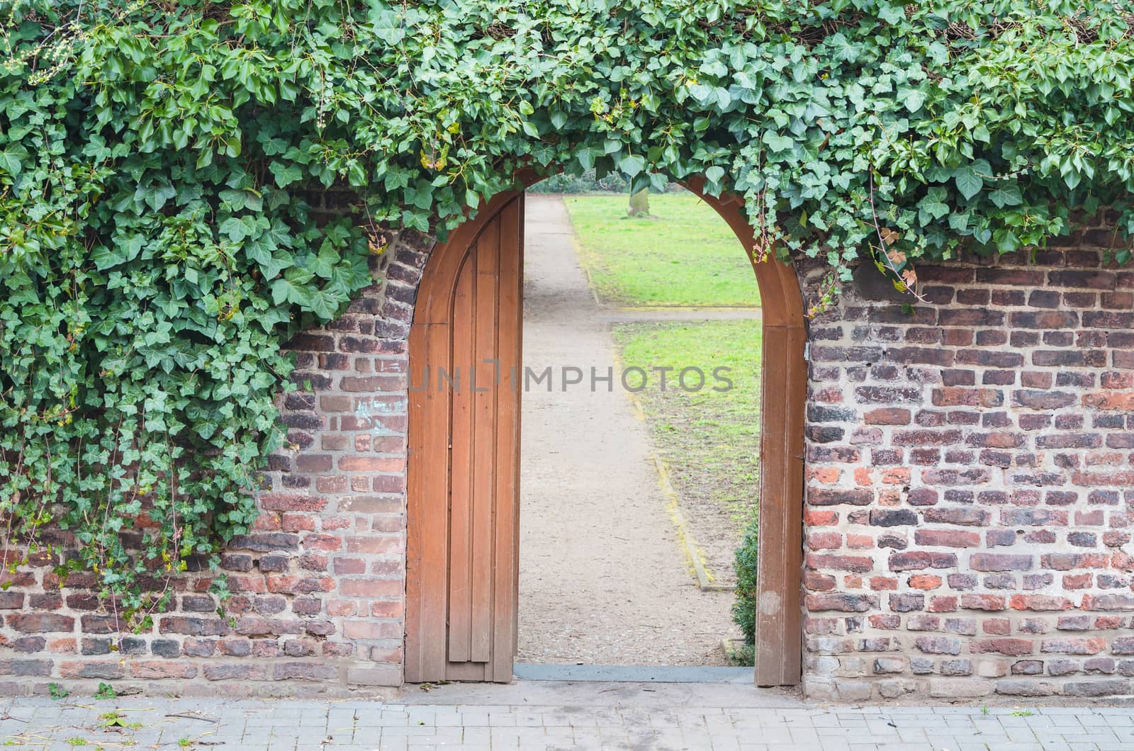 An entrance gate in a wall into a park. Behind the open door is a way.
