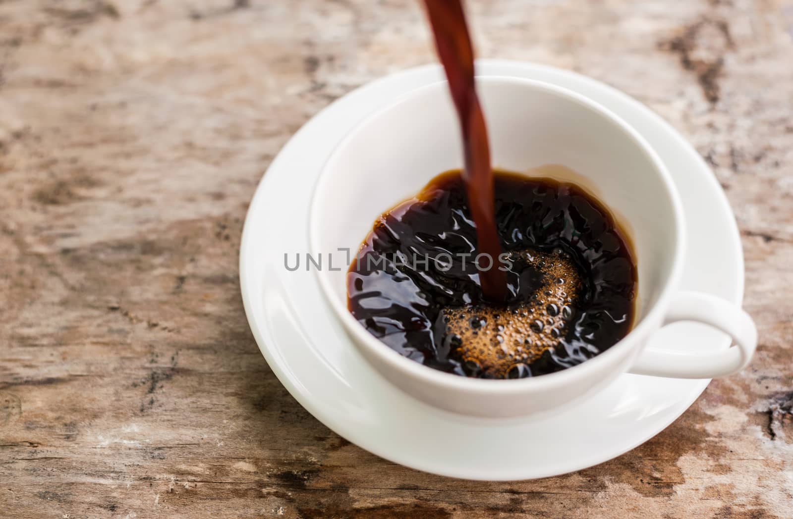 Coffee splash into a cup of coffee. On a wooden background