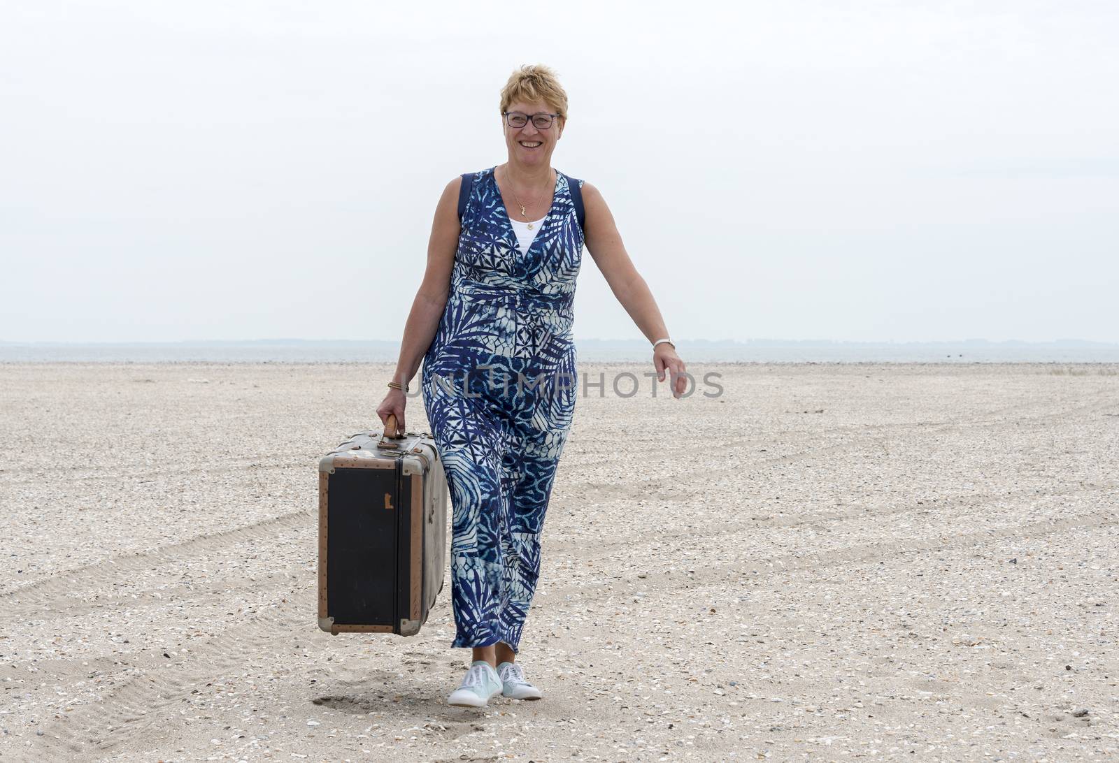 woman with old vintage used suitcase walking on the beach