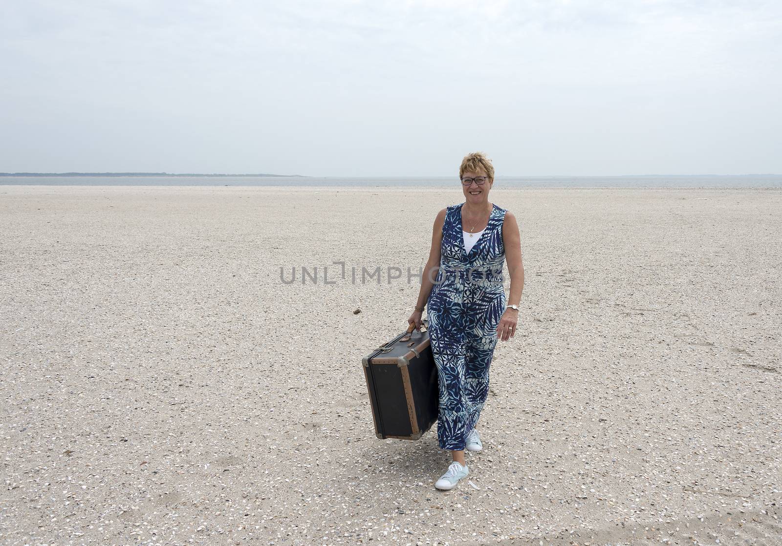 woman with suitcase walking on the beach