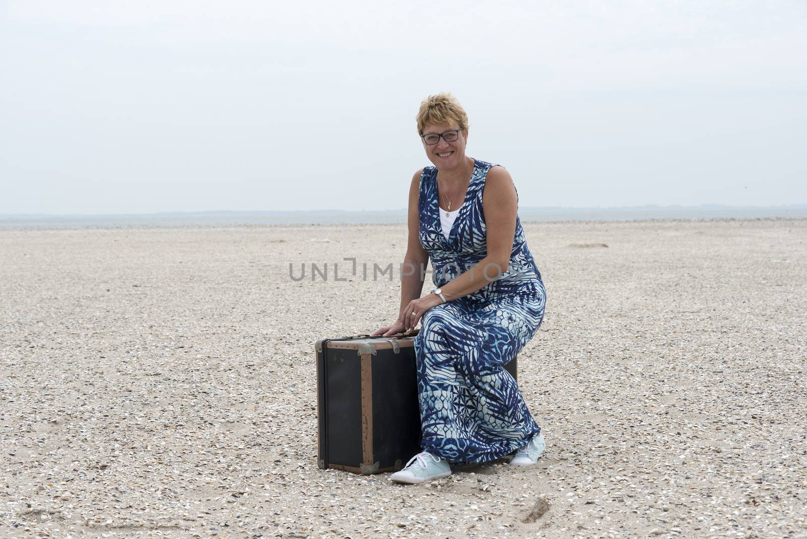 woman sitting on suitcase on the sandy beach