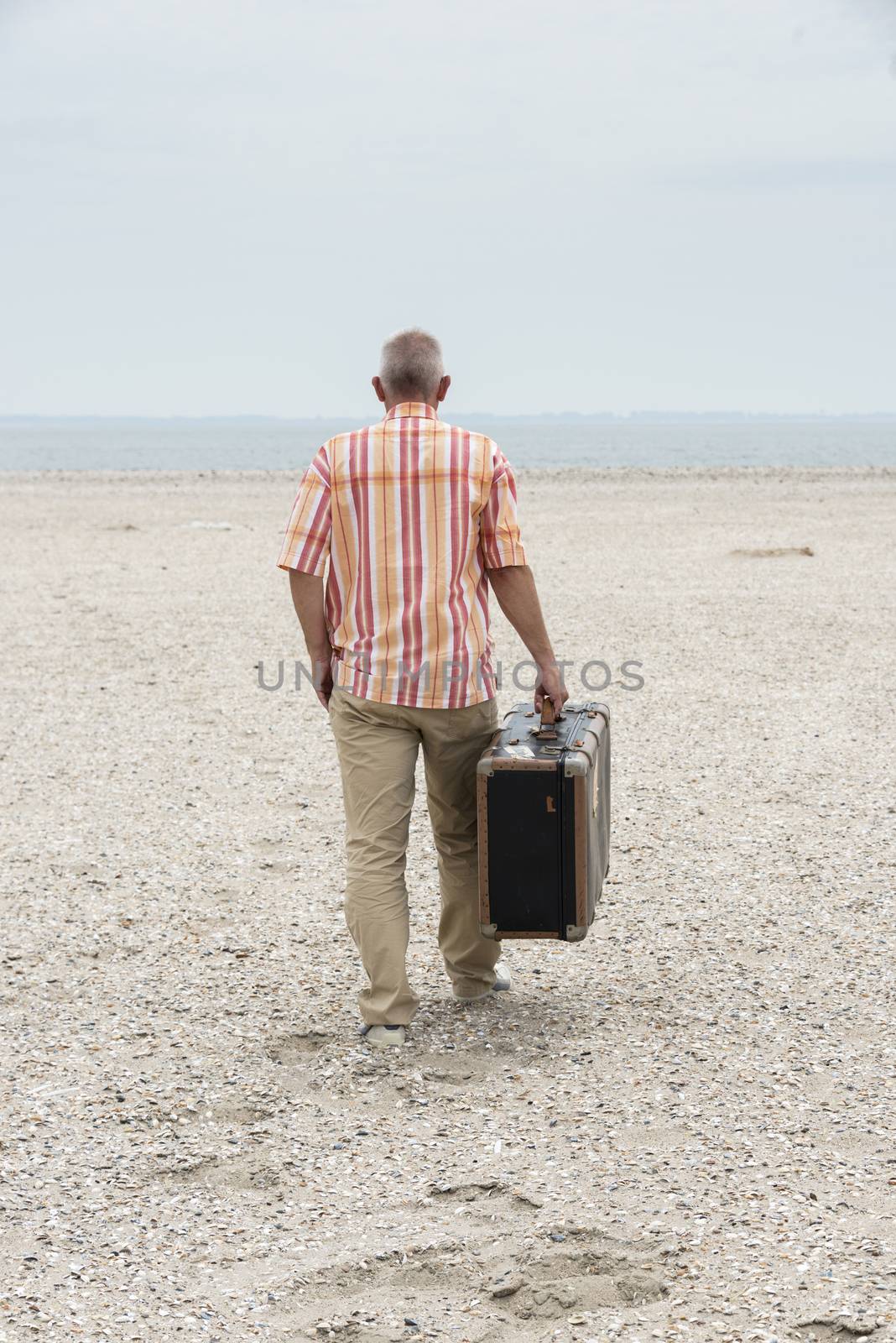 man with old vintage used suitcase walking on the beach
