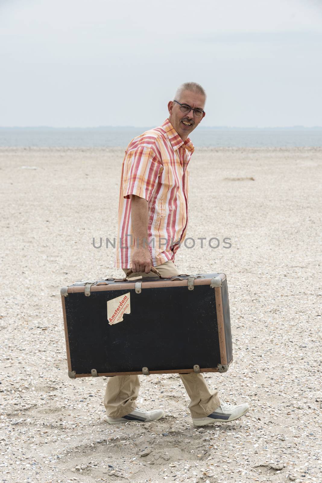 man with old vintage used suitcase walking on the beach