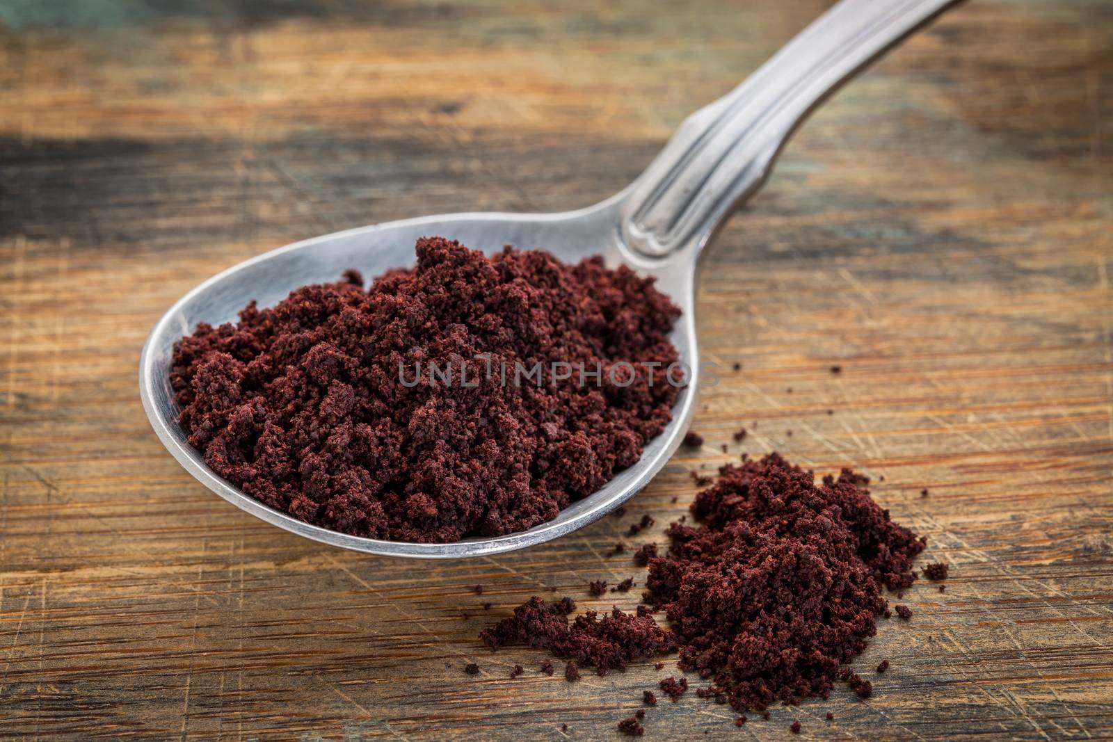 acai berry powder on tablespoon against rustic wooden cutting board