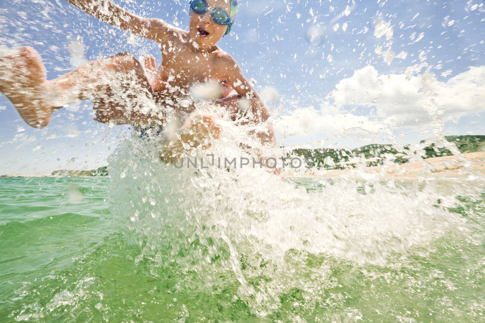 Splashes over an excited kid, thrown in to the see water by his father on a sunny day at the beach.