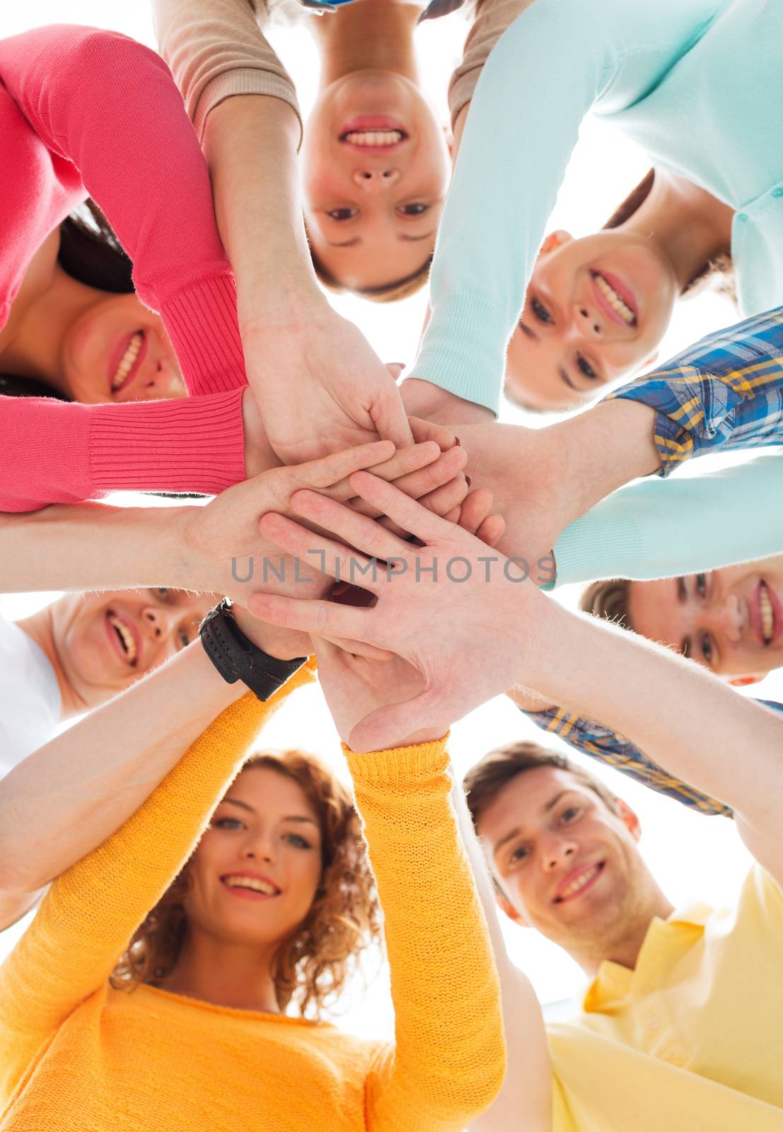 friendship, youth and people concept - group of smiling teenagers with hands on top of each other