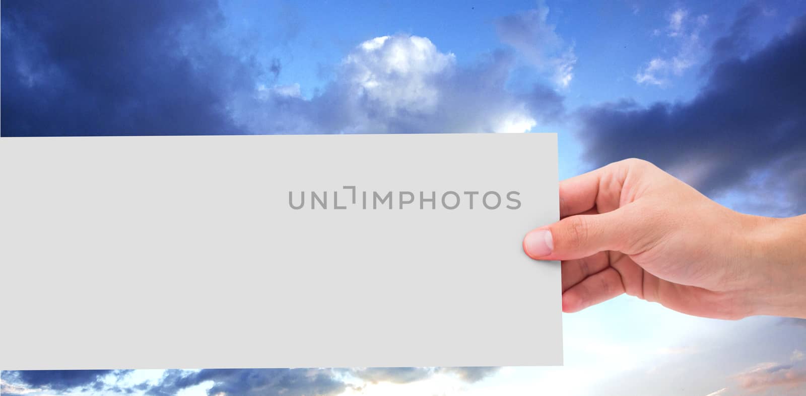 Hand showing card against blue and orange sky with clouds