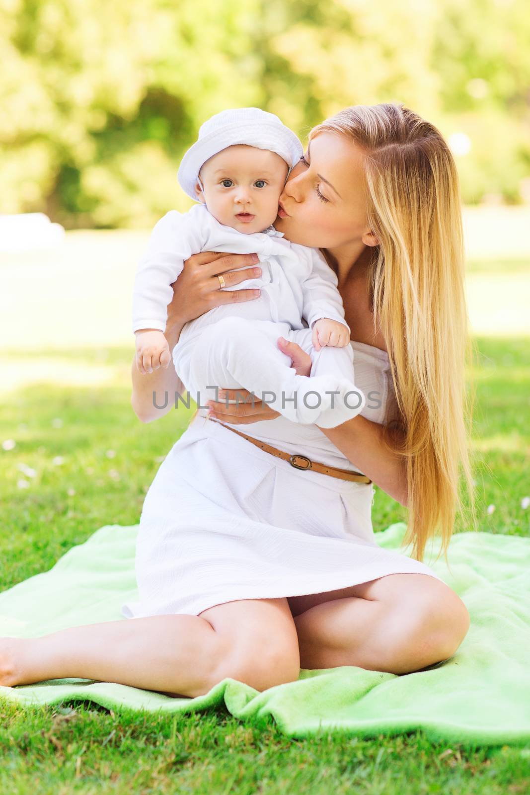 family, child and parenthood concept - happy mother kissing her little baby and sitting on blanket in park