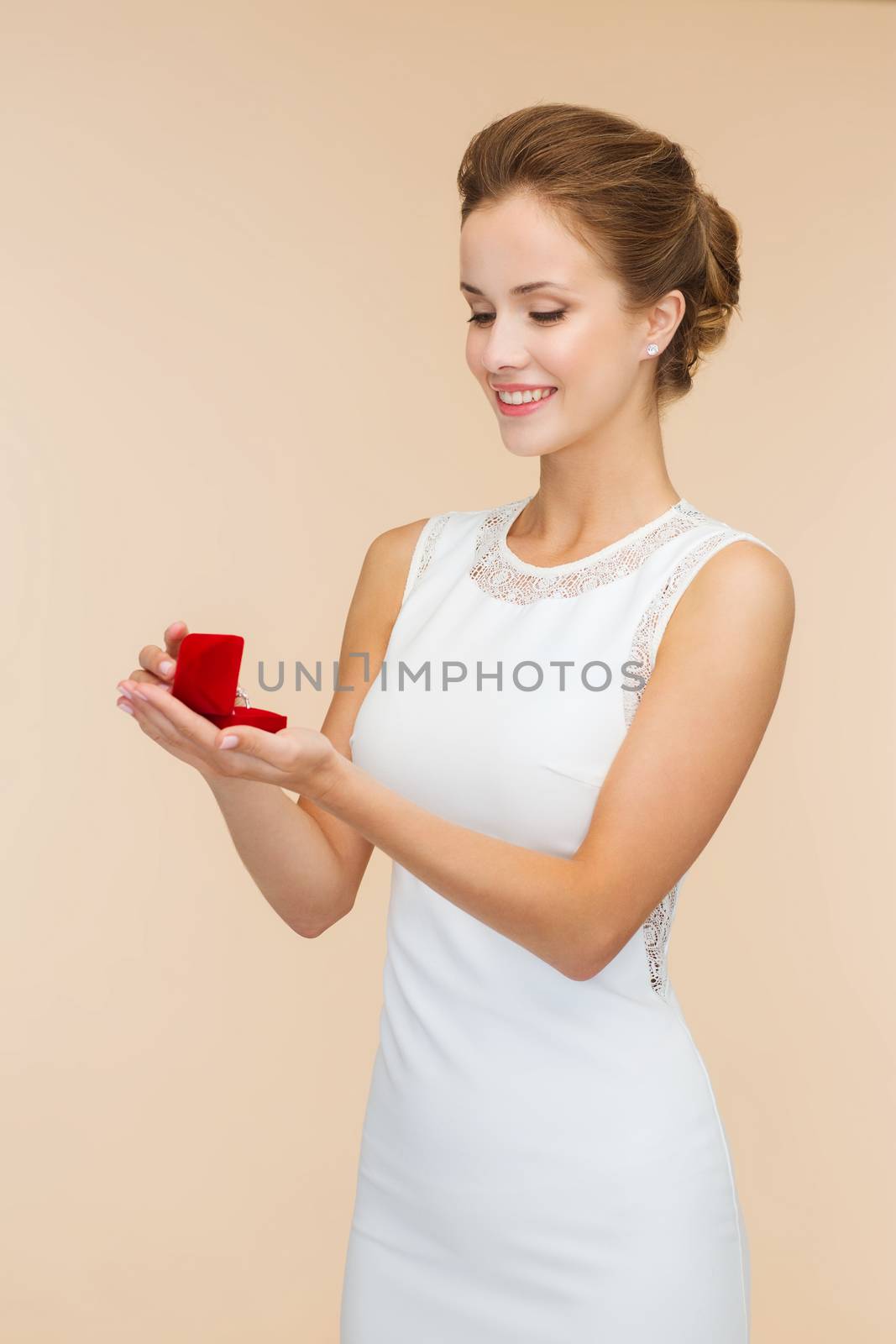 wedding, love, engagement and happiness concept - smiling woman in white dress holding red gift box with diamond ring over beige background