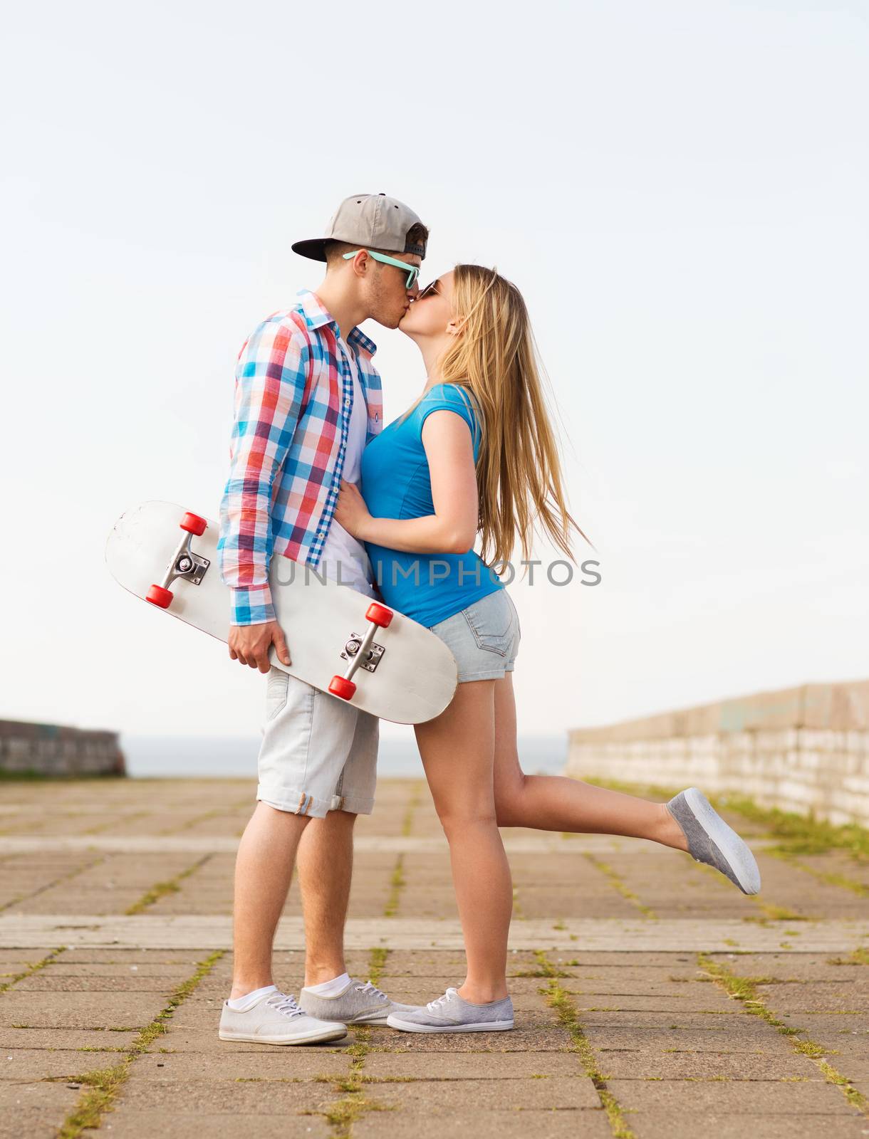 holidays, vacation, love and friendship concept - smiling couple with skateboard kissing outdoors