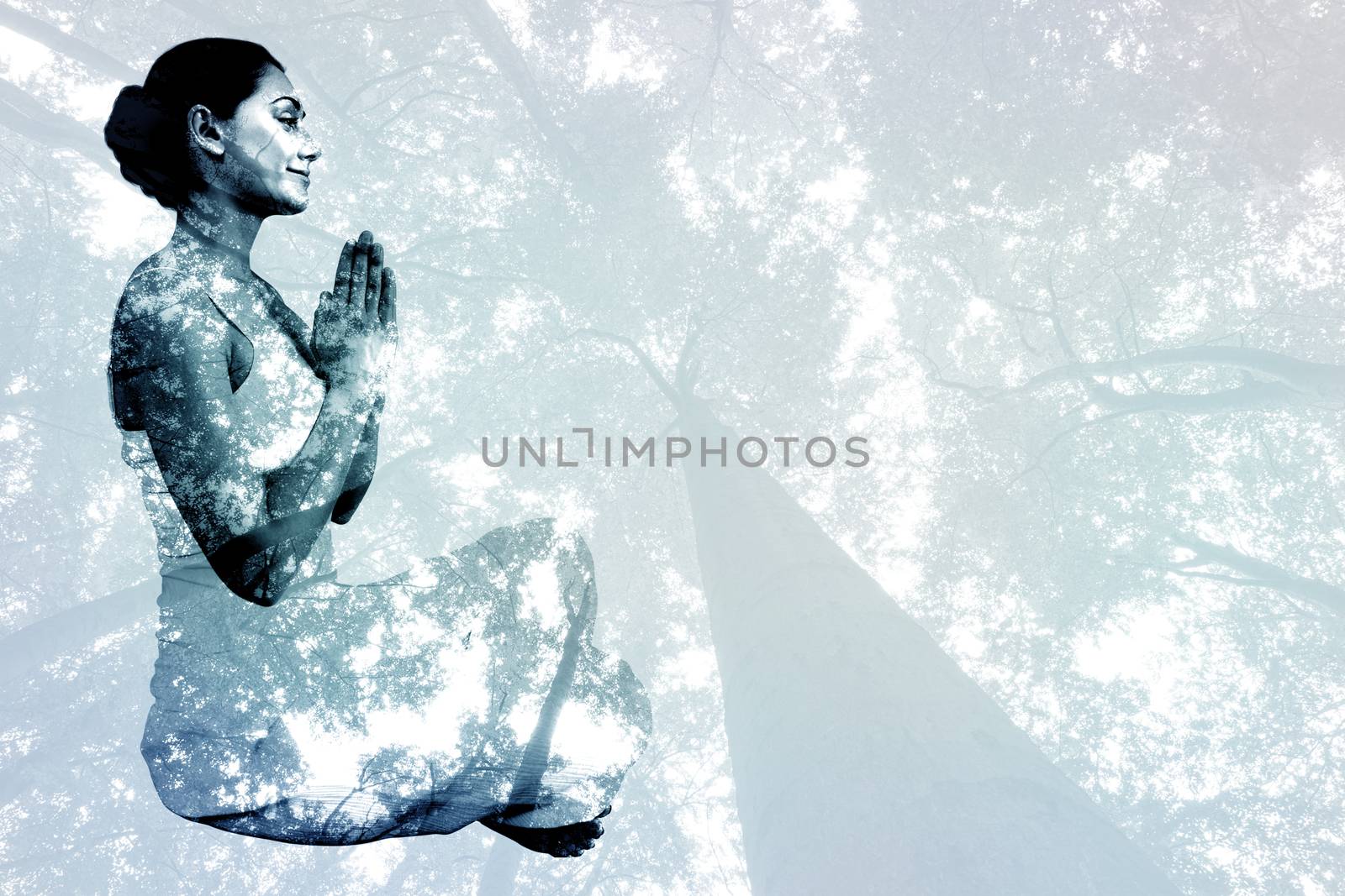 Content brunette in white sitting in lotus pose  against low angle view of tall trees