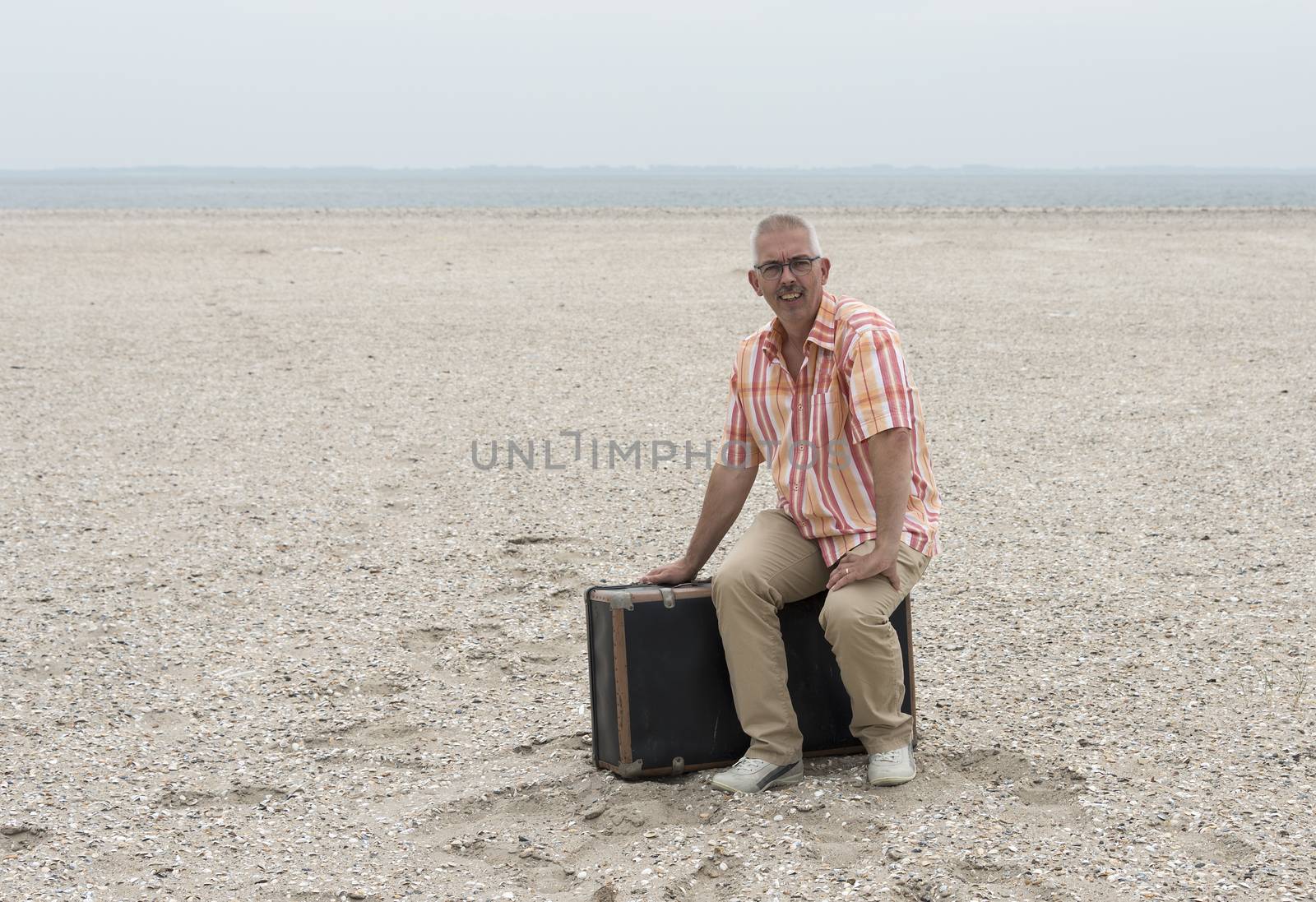 man traveling with old suitcase sitting on the beach