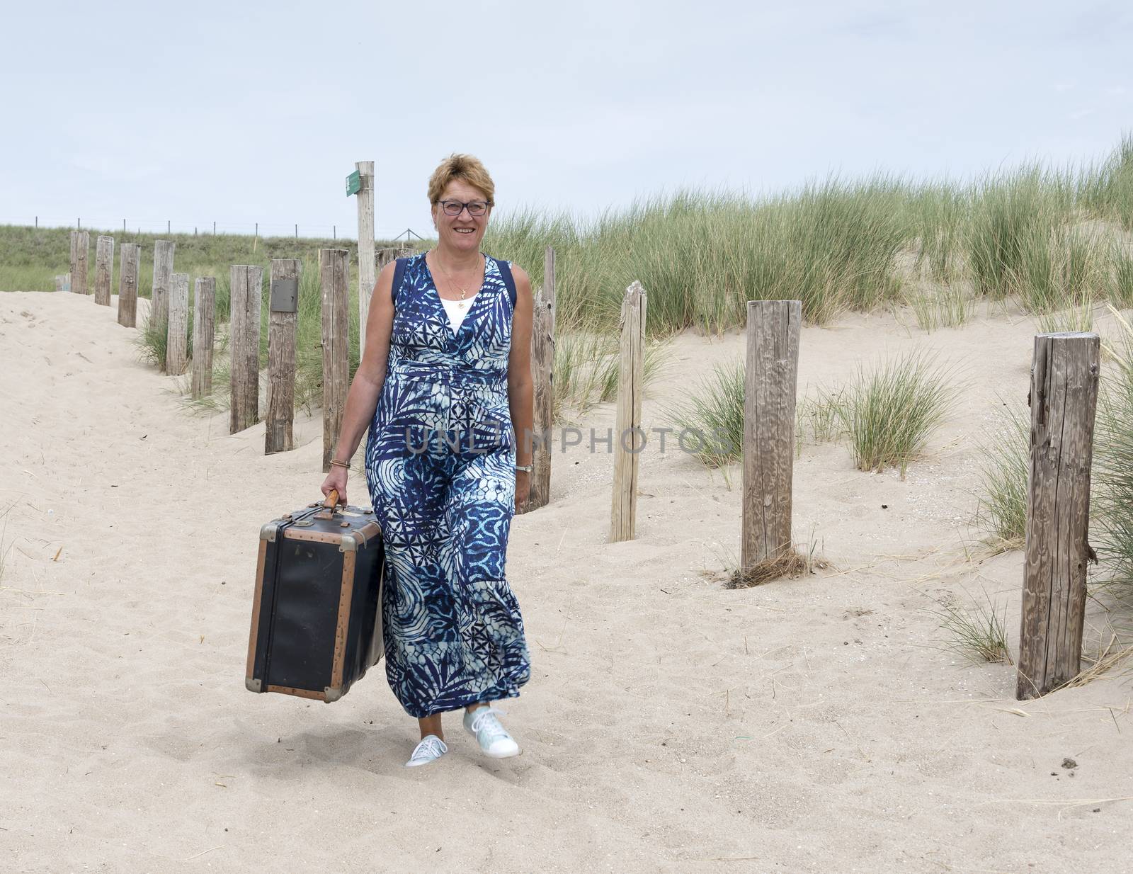 woman walking with heavy old leather suitcase on the beach
