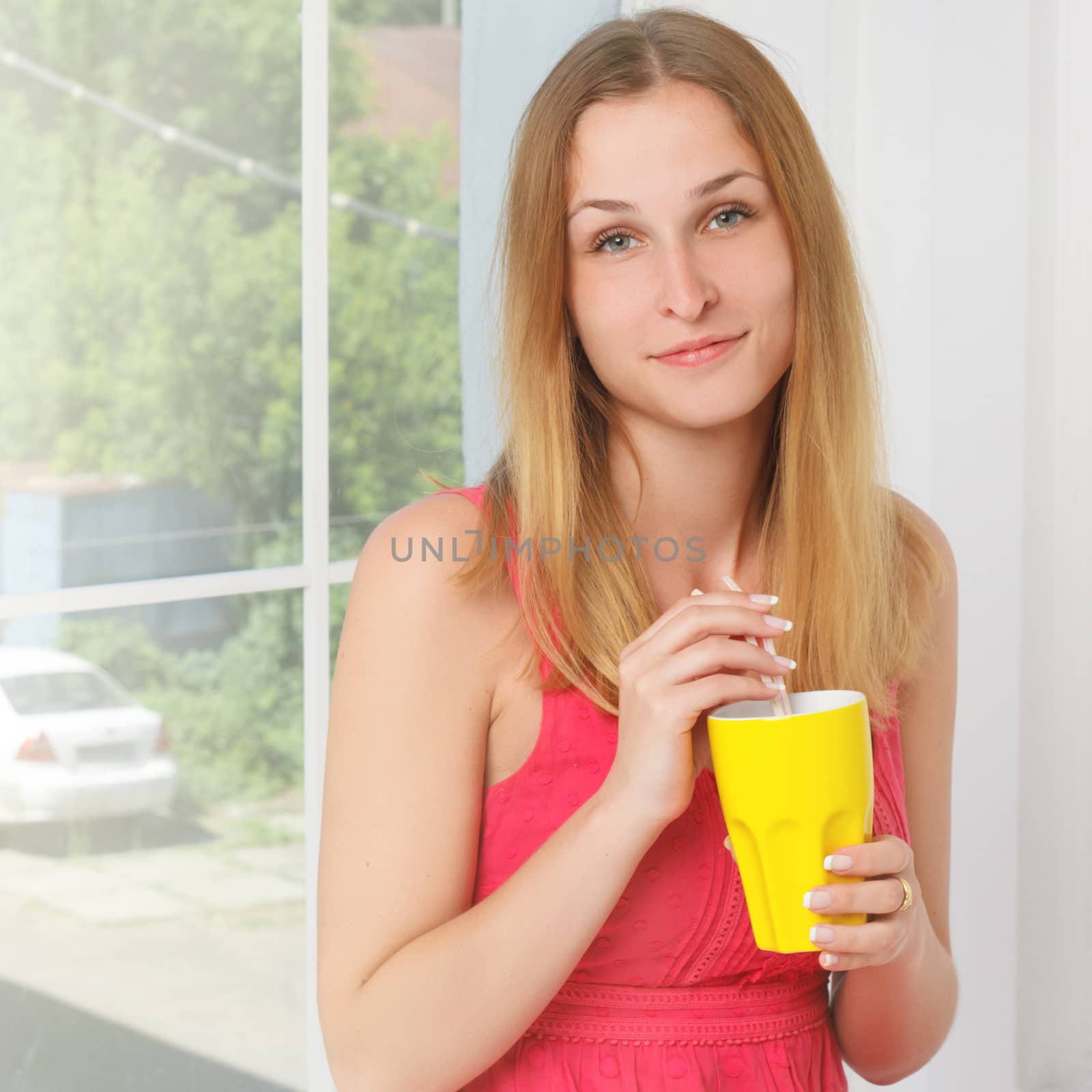 girl in a pink dress with yellow glass in hand at home near a window
