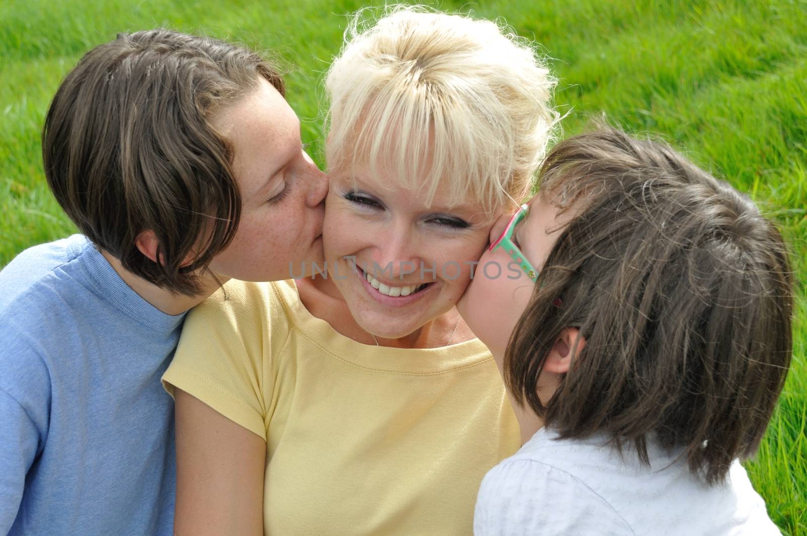 A mother smiles as she receives a kiss on the cheek from her young daughters