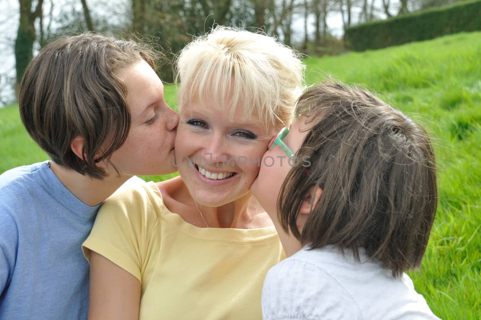 A mother smiles as she receives a kiss on the cheek from her young daughters