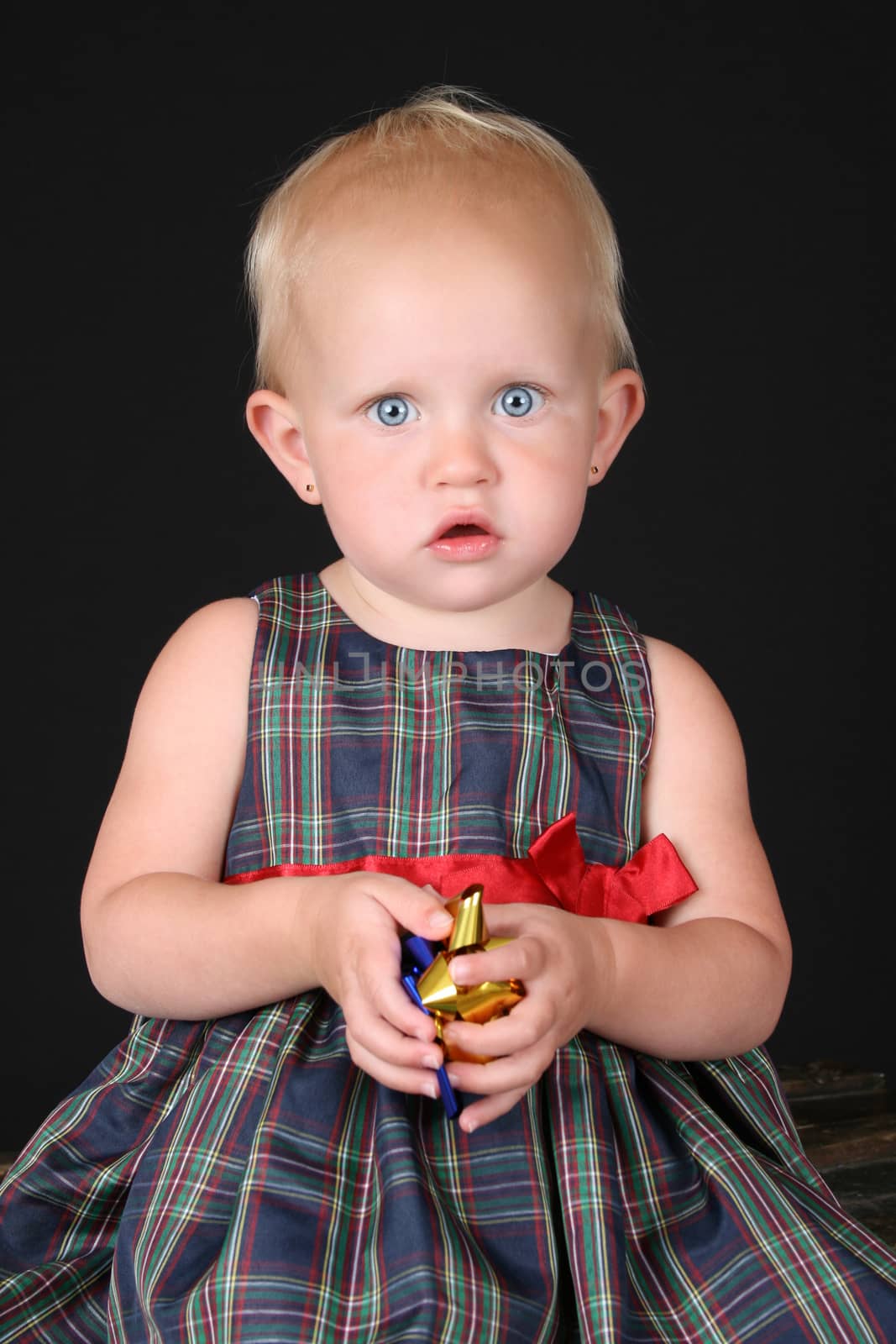 Blonde toddler girl wearing a christmas dress against black