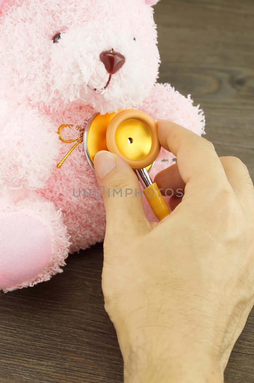 Hand of man holding stethoscope to examination the pink doll.                           