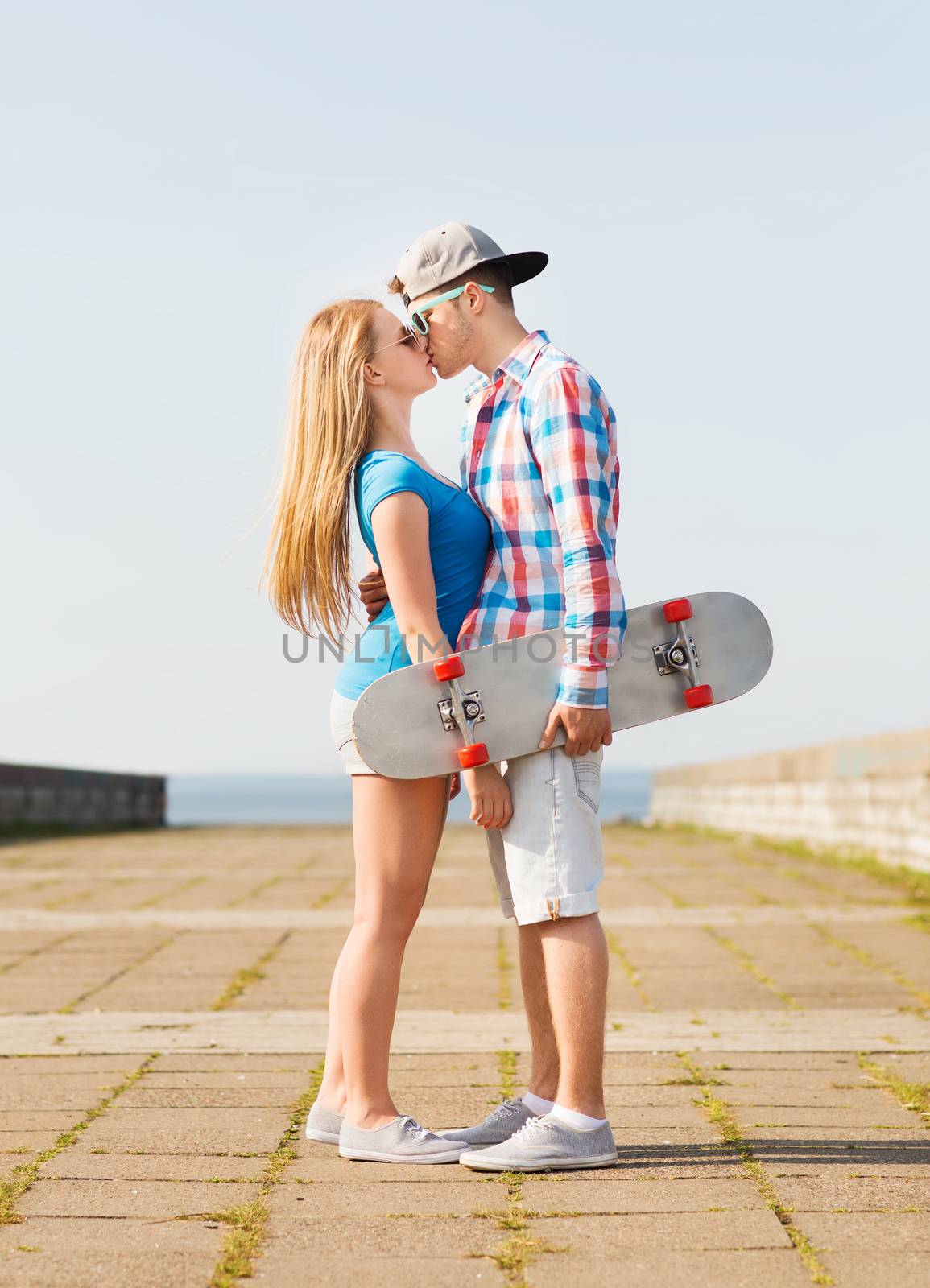 holidays, vacation, love and friendship concept - smiling couple with skateboard kissing outdoors