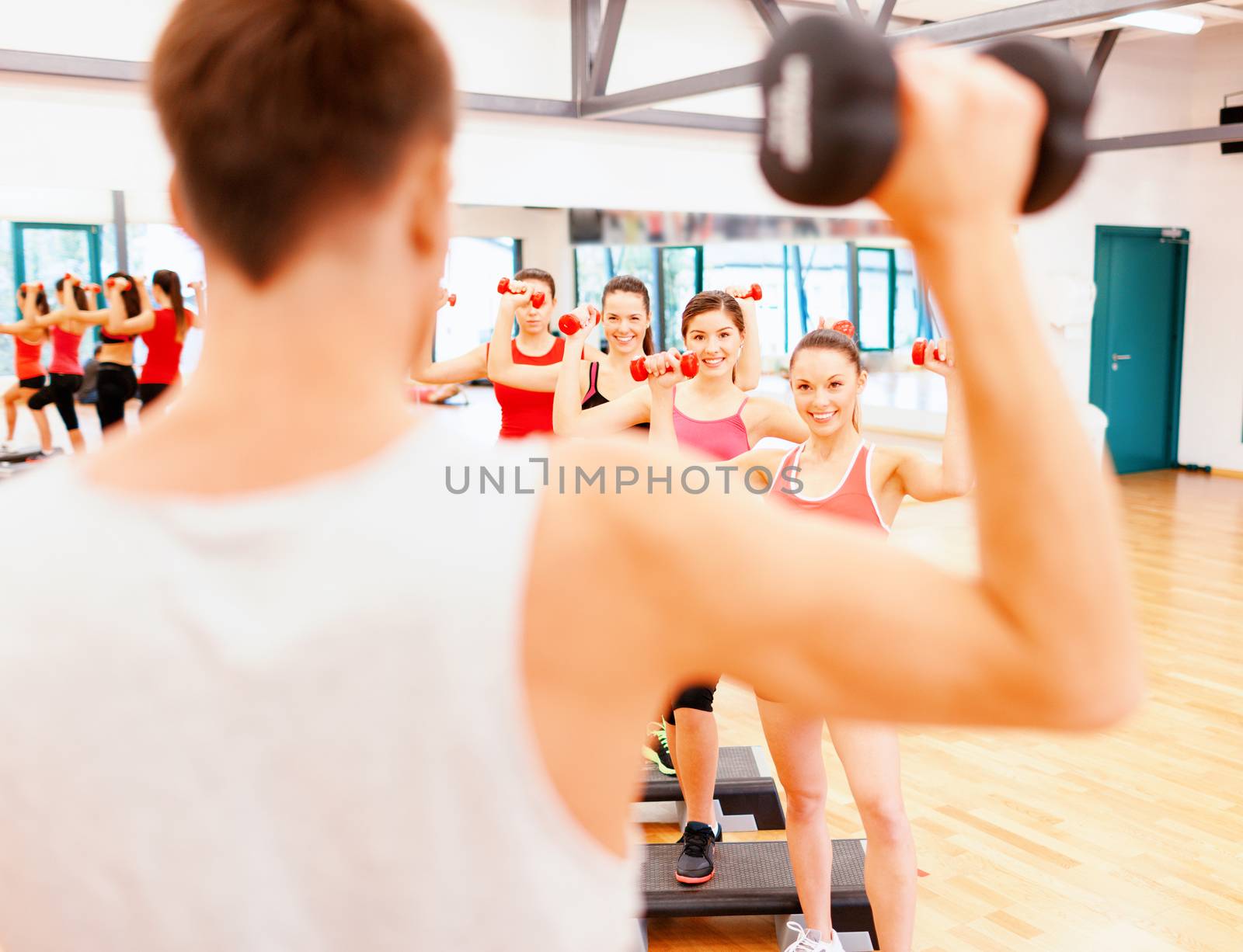 fitness, sport, training, gym and lifestyle concept - group of smiling female with dumbbells and aerobic step an trainer infront