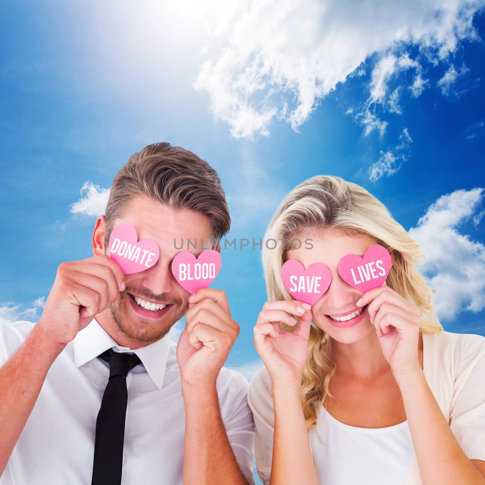 Attractive young couple holding pink hearts over eyes against blue sky