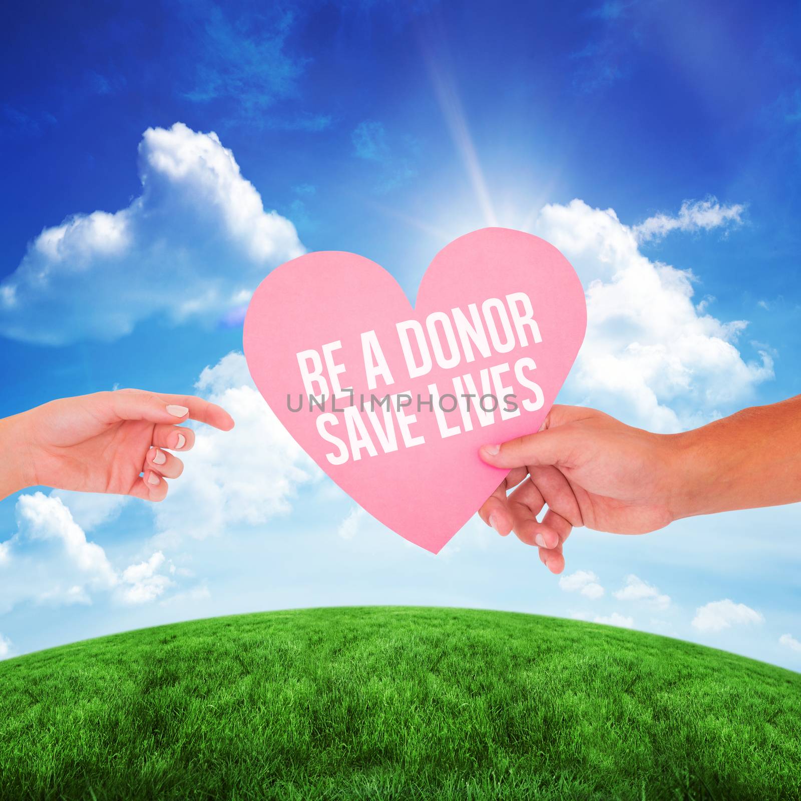 Couple passing a paper heart against green hill under blue sky