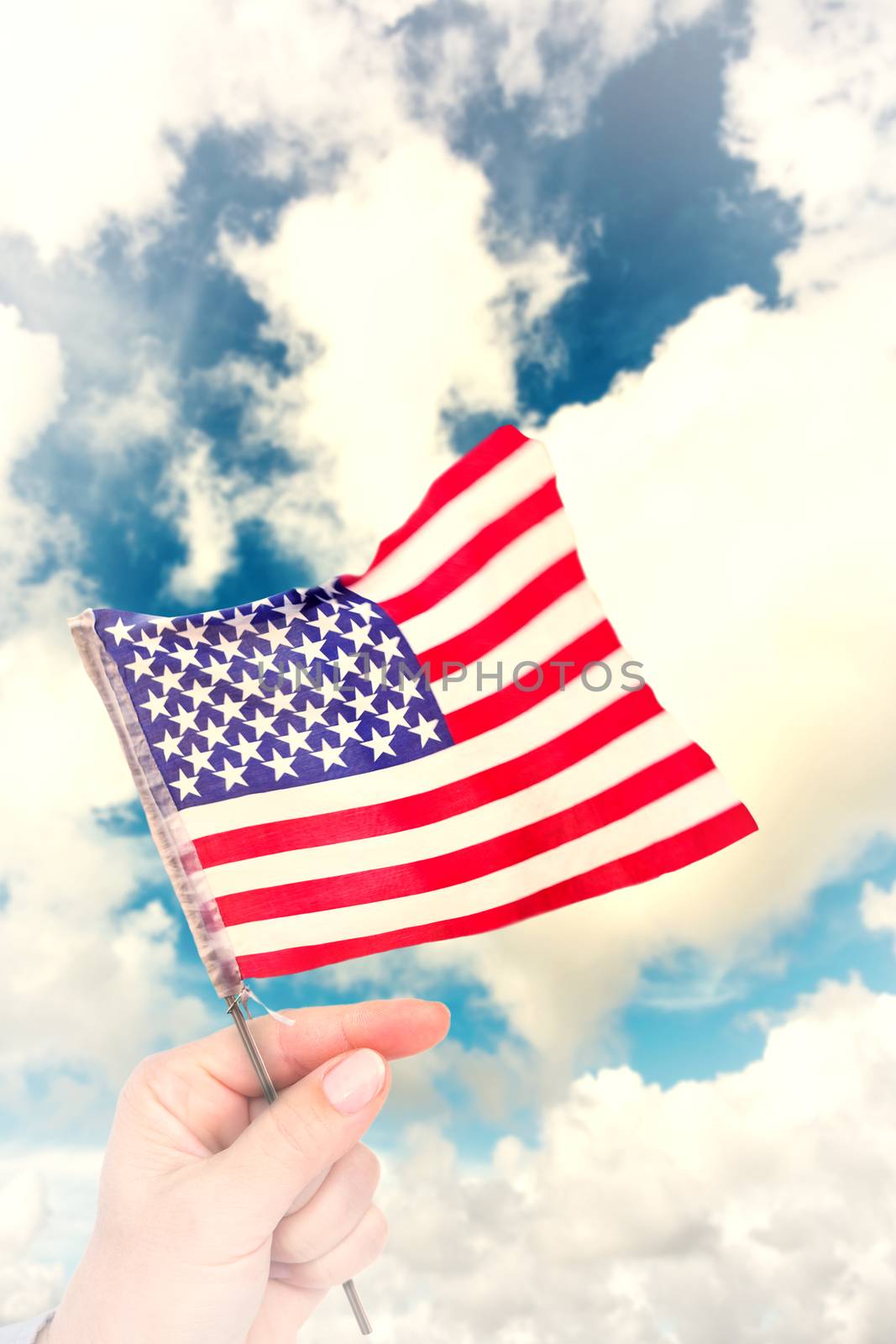 Hand waving american flag against blue sky with white clouds