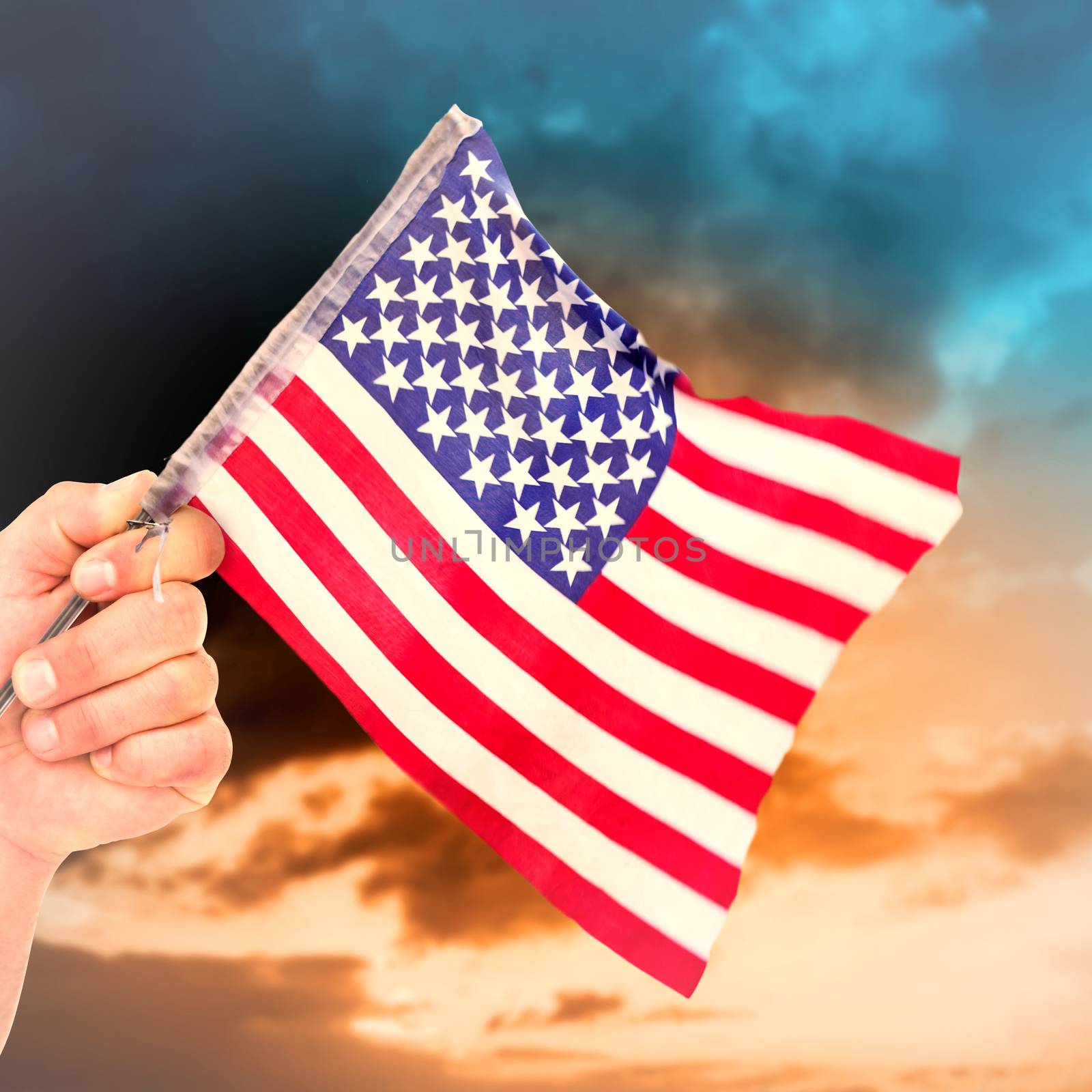 Hand waving american flag against green grass under blue and orange sky