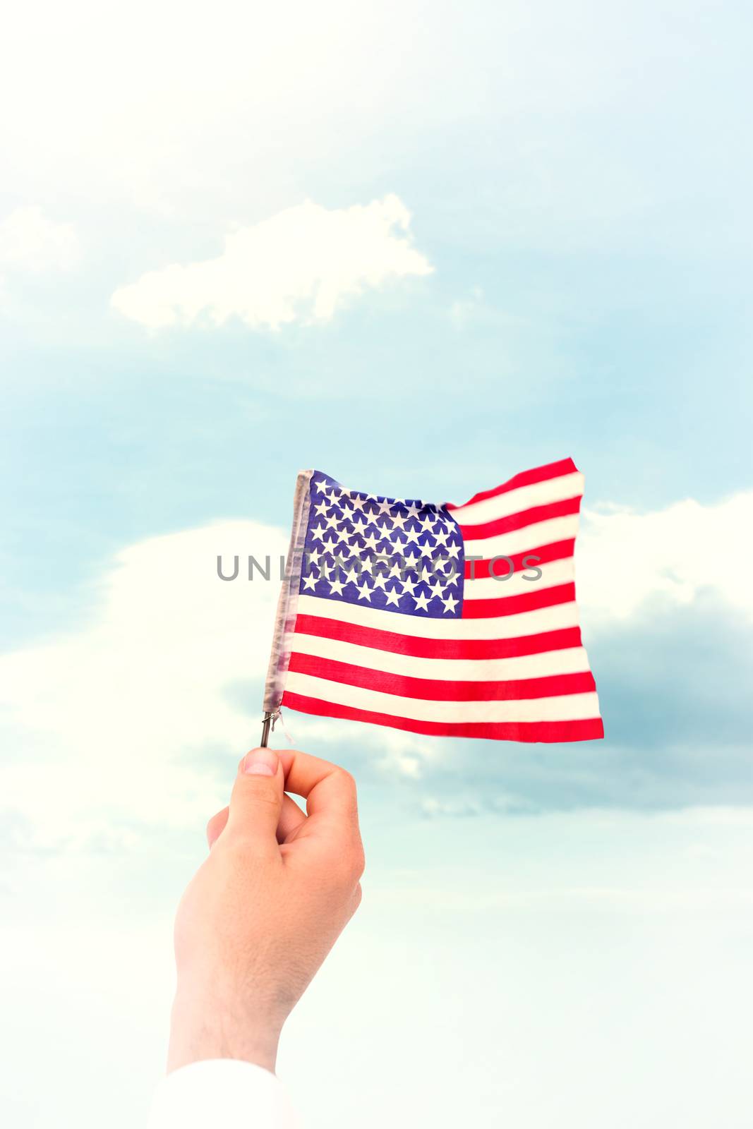 Hand waving american flag against blue sky