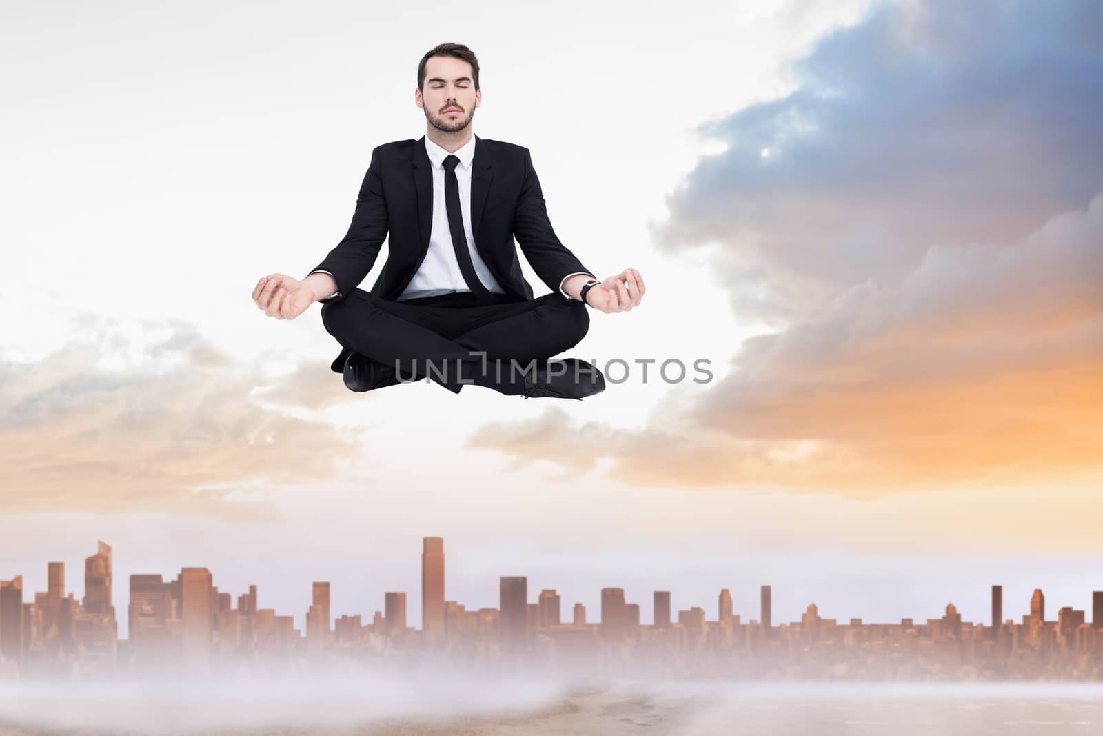 Peaceful businessman sitting in lotus pose relaxing against sandy path leading to large urban city
