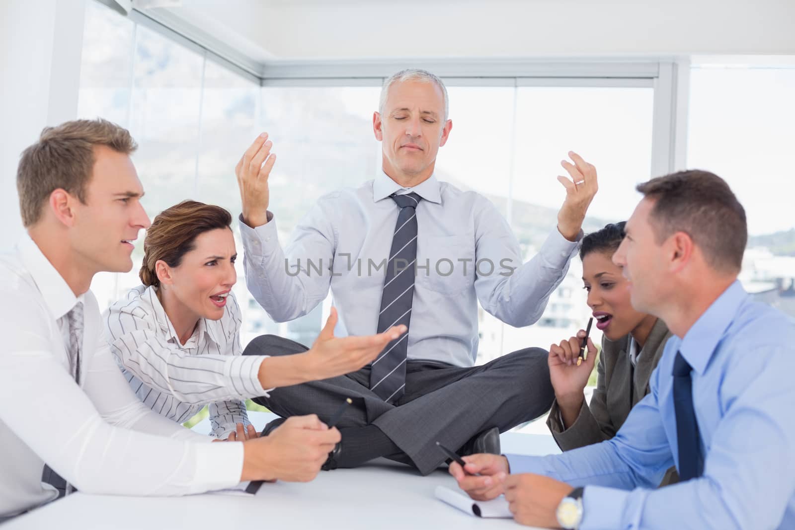 Businessman relaxing on the desk with upset colleagues around in the office