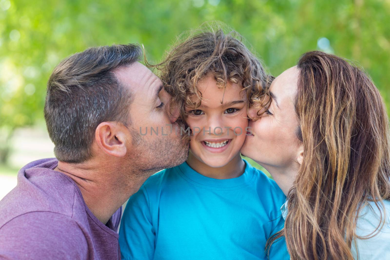 Happy family kissing at camera in the park on a sunny day