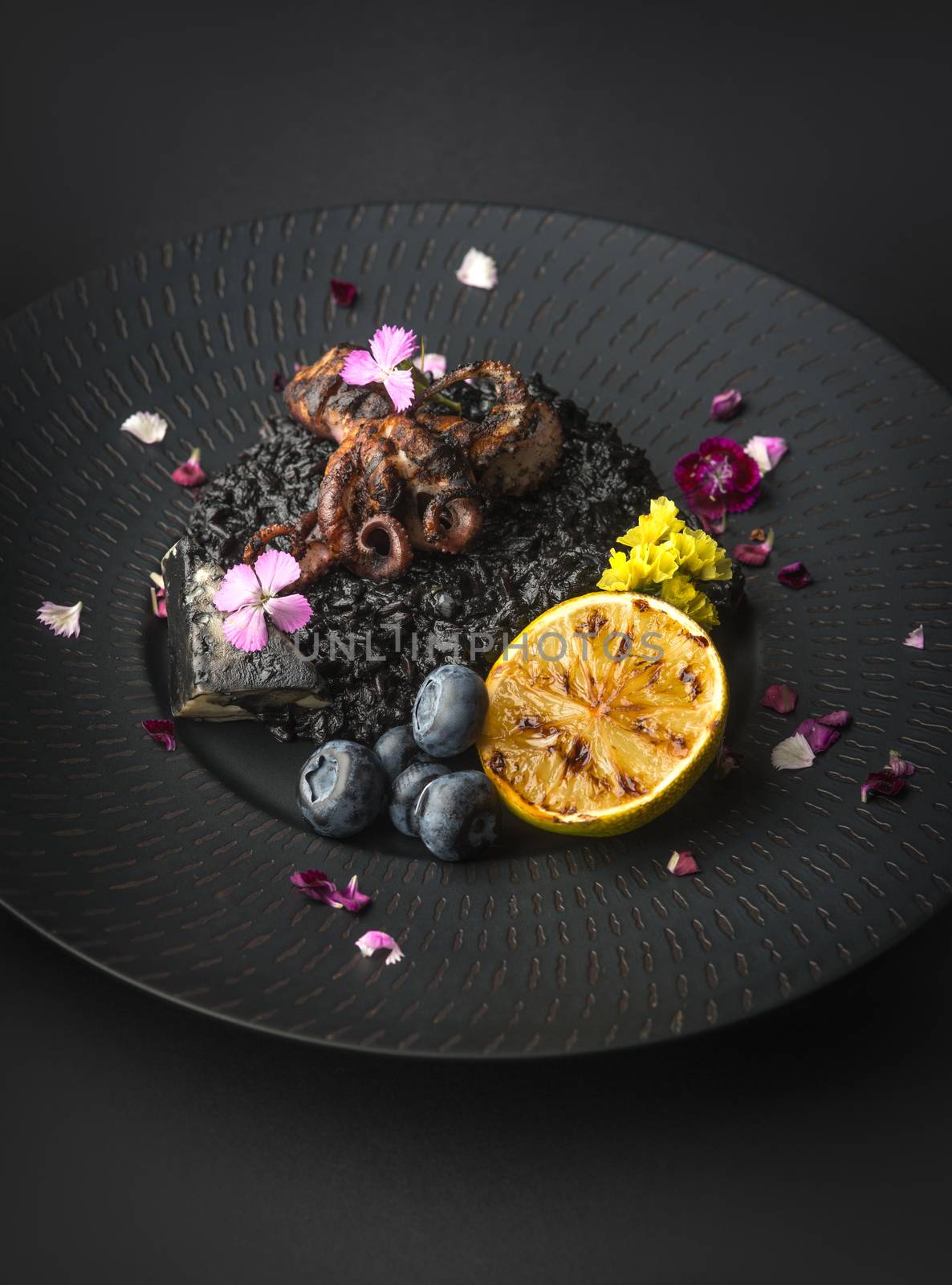 risotto with octopus and blueberries on a black plate on a black background
