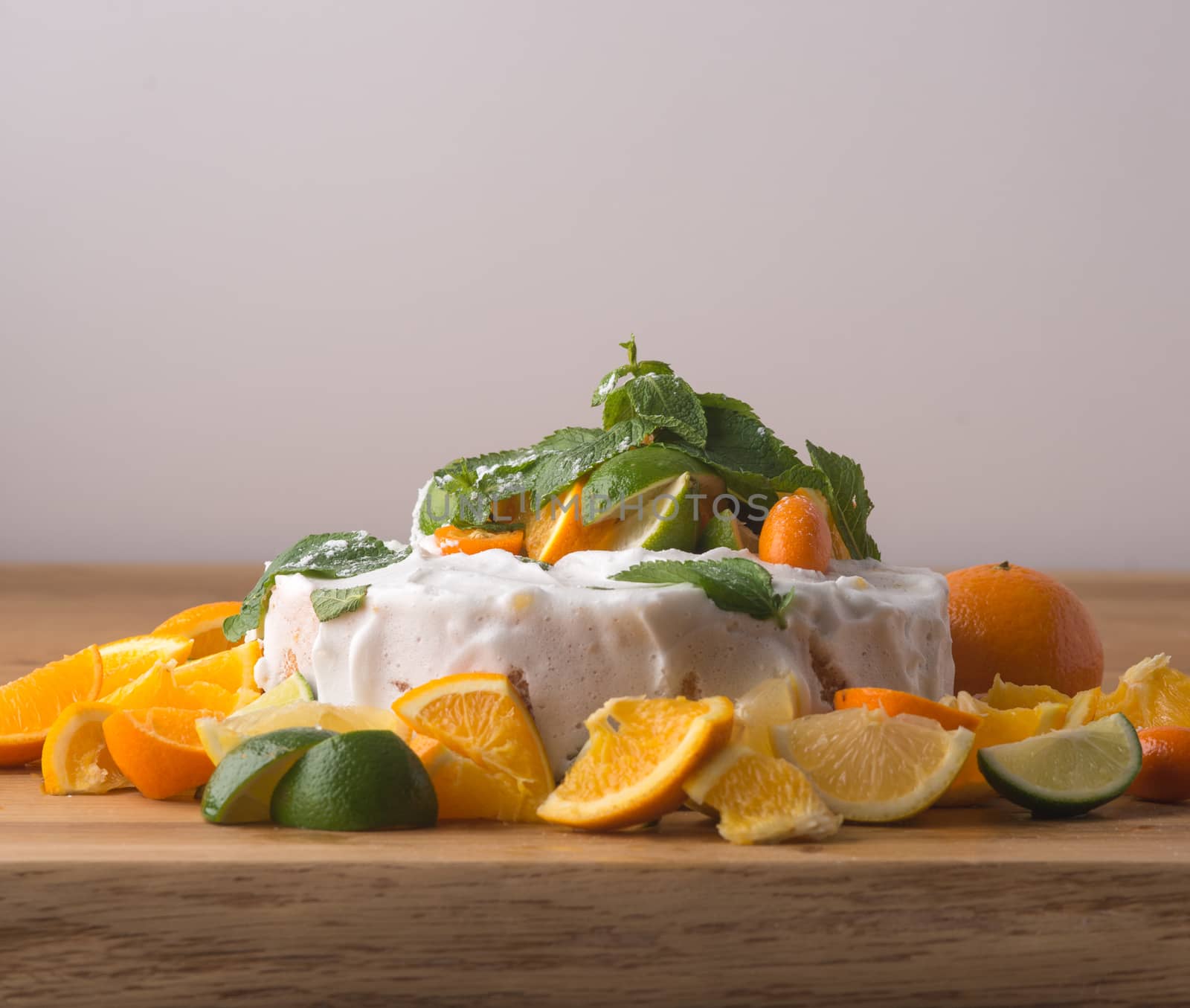 Fruit cake with cream, lime and oranges on table with light background