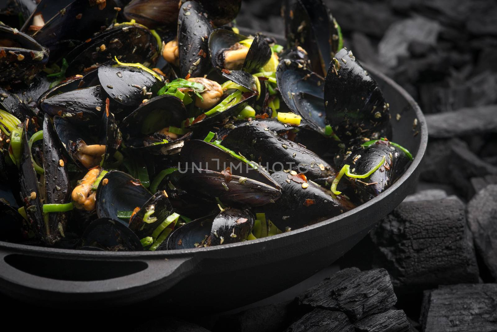 Steamed Mussels with vegetables in a black frying pan on the coa by shivanetua