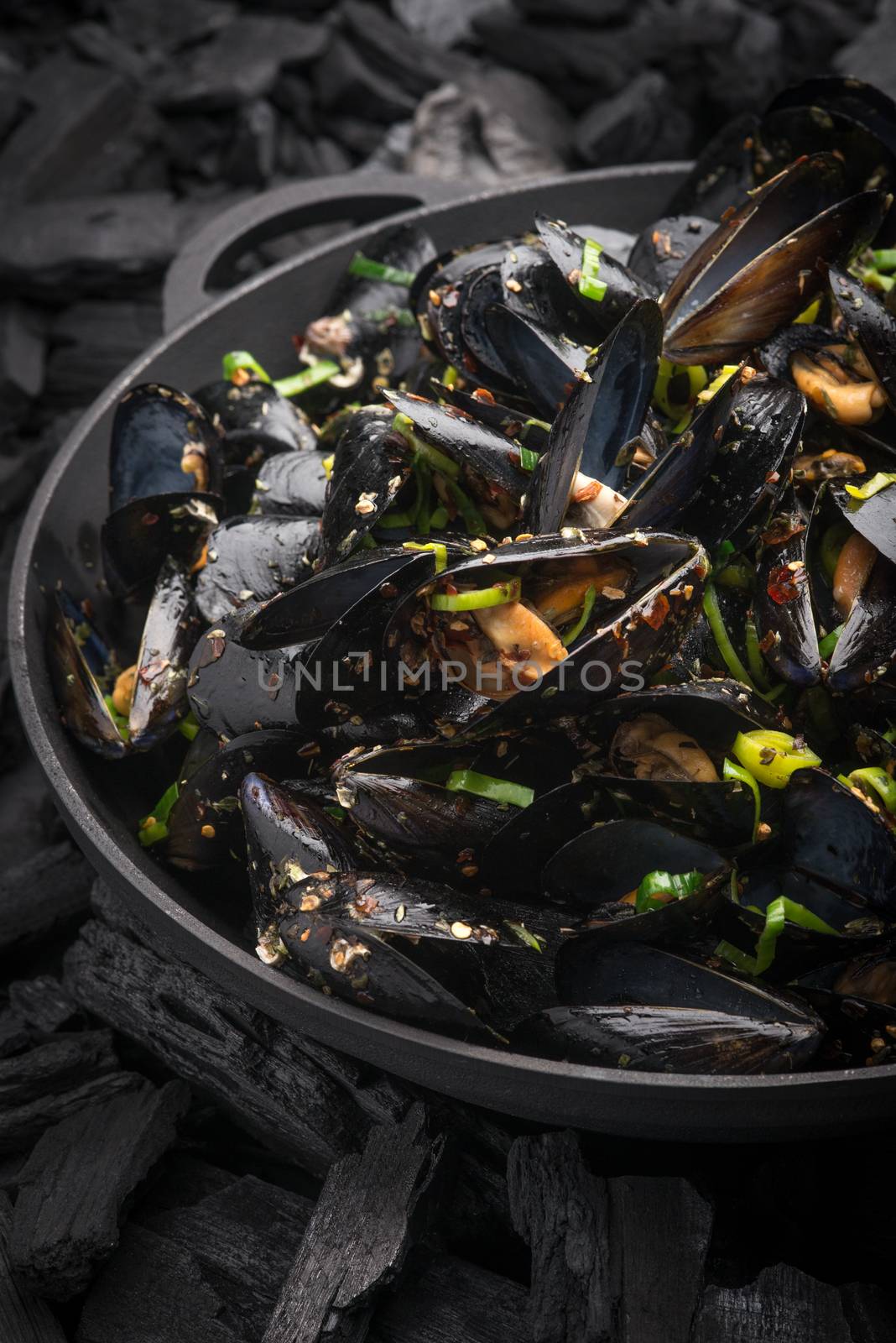 Steamed Mussels with vegetables in a black frying pan on the coals