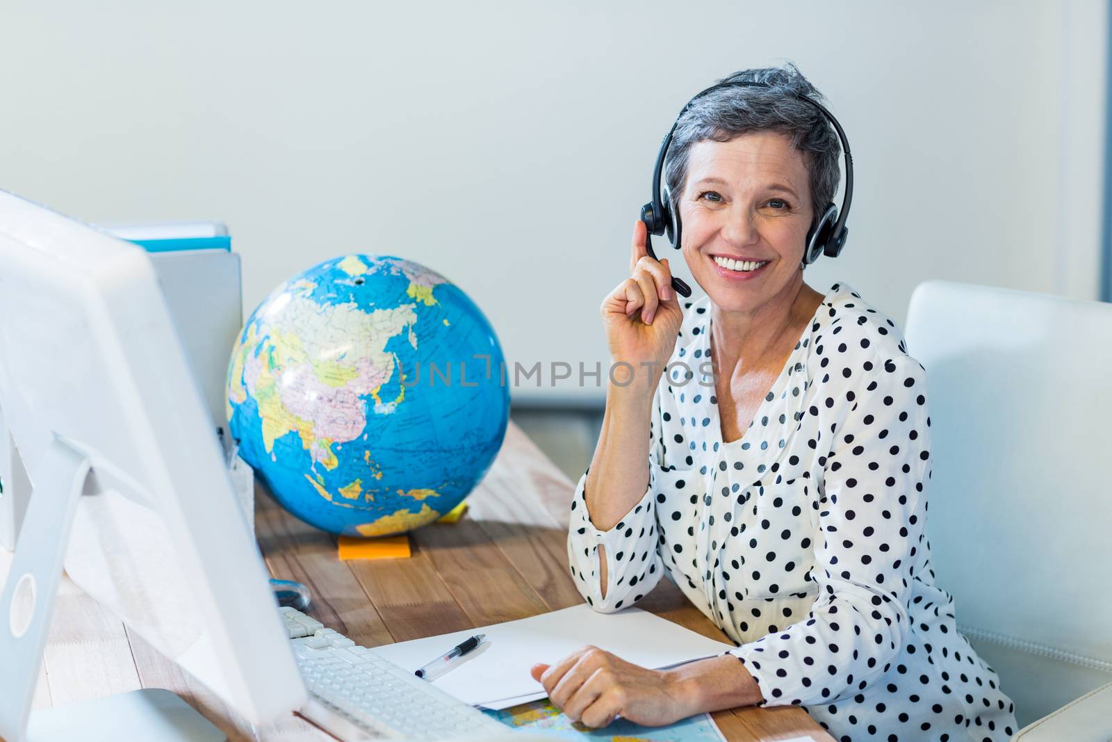 Smiling travel agent sitting at her desk by Wavebreakmedia