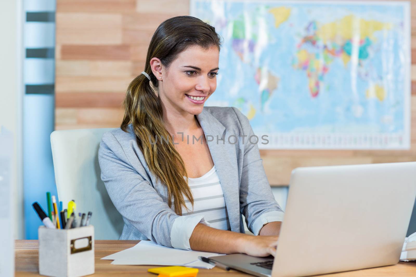 Pretty travel agent working on laptop in the office