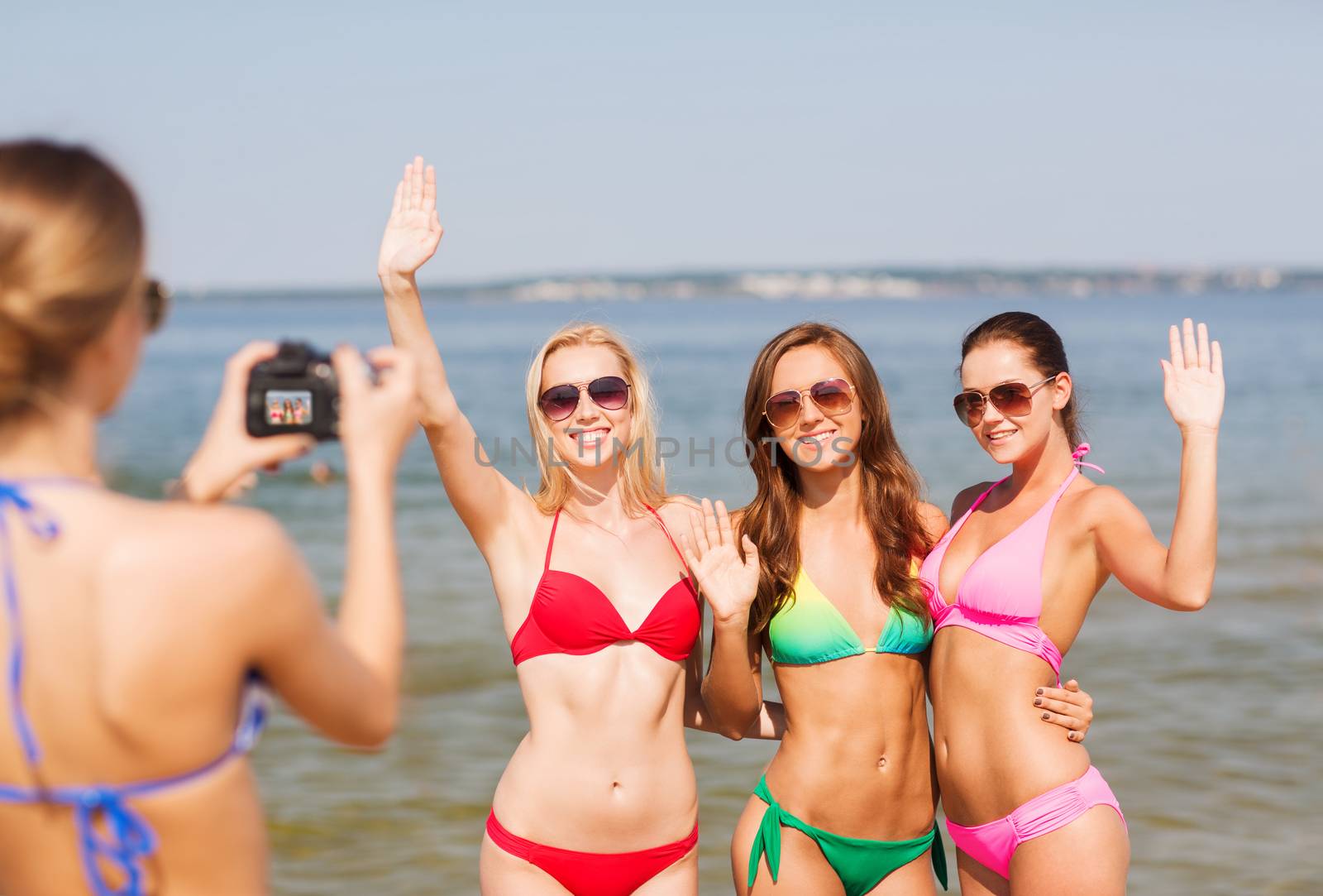 group of smiling women photographing on beach by dolgachov