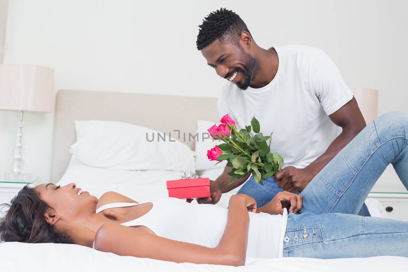 Romantic man giving roses to partner at home in bedroom