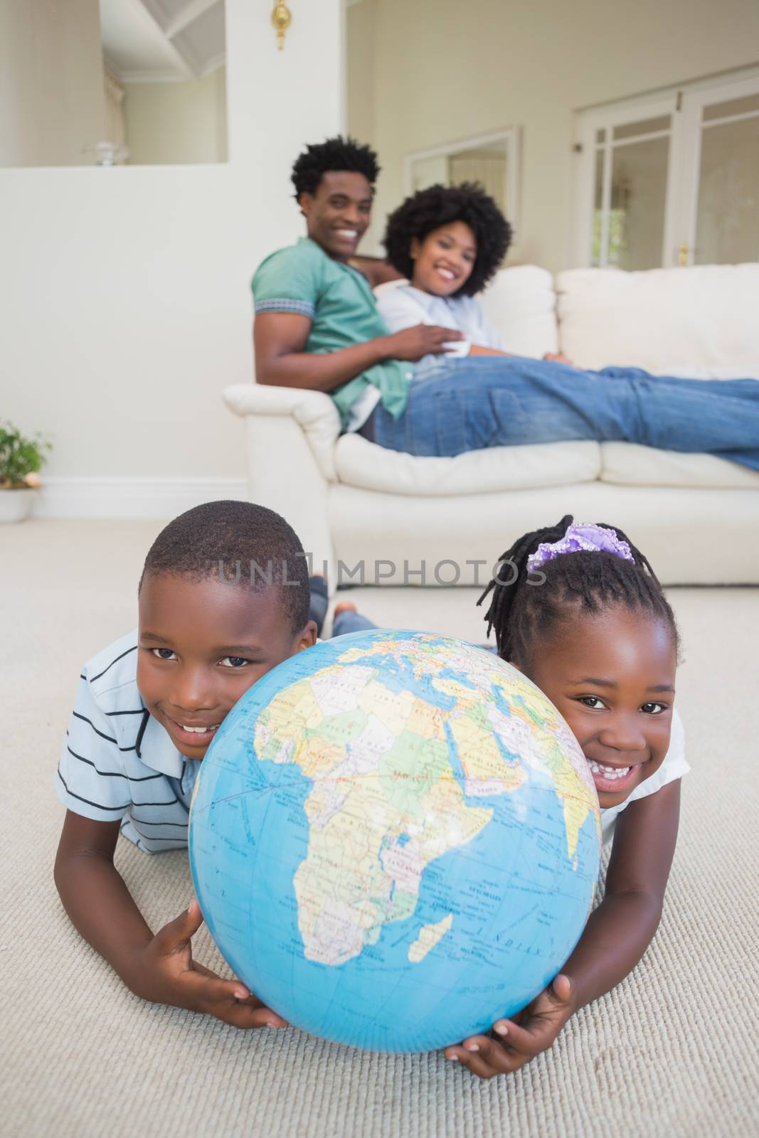 Happy siblings lying on the floor holding globe at home in the living room