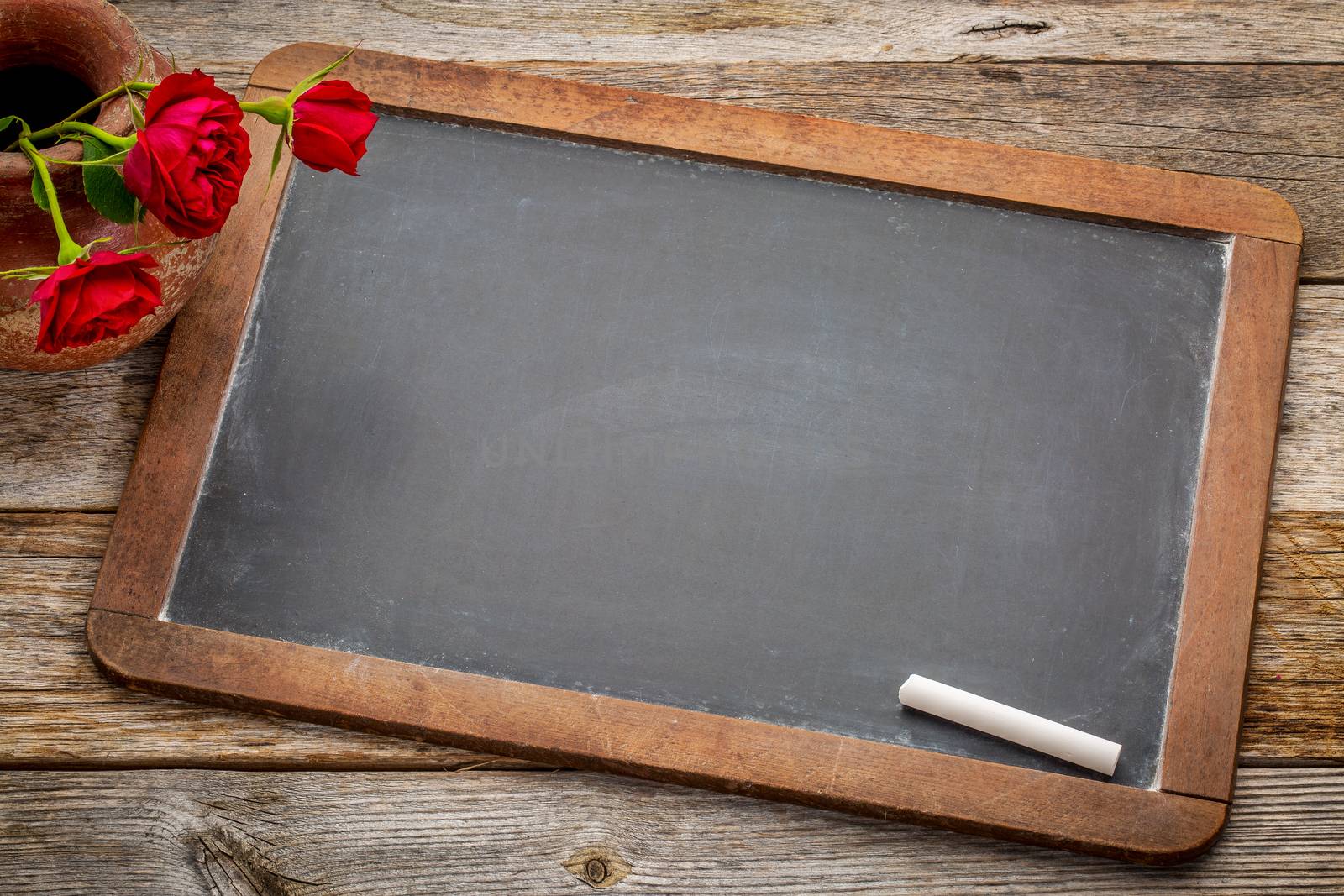blank vintage slate  blackboard with white chalk and red roses against rustic wood
