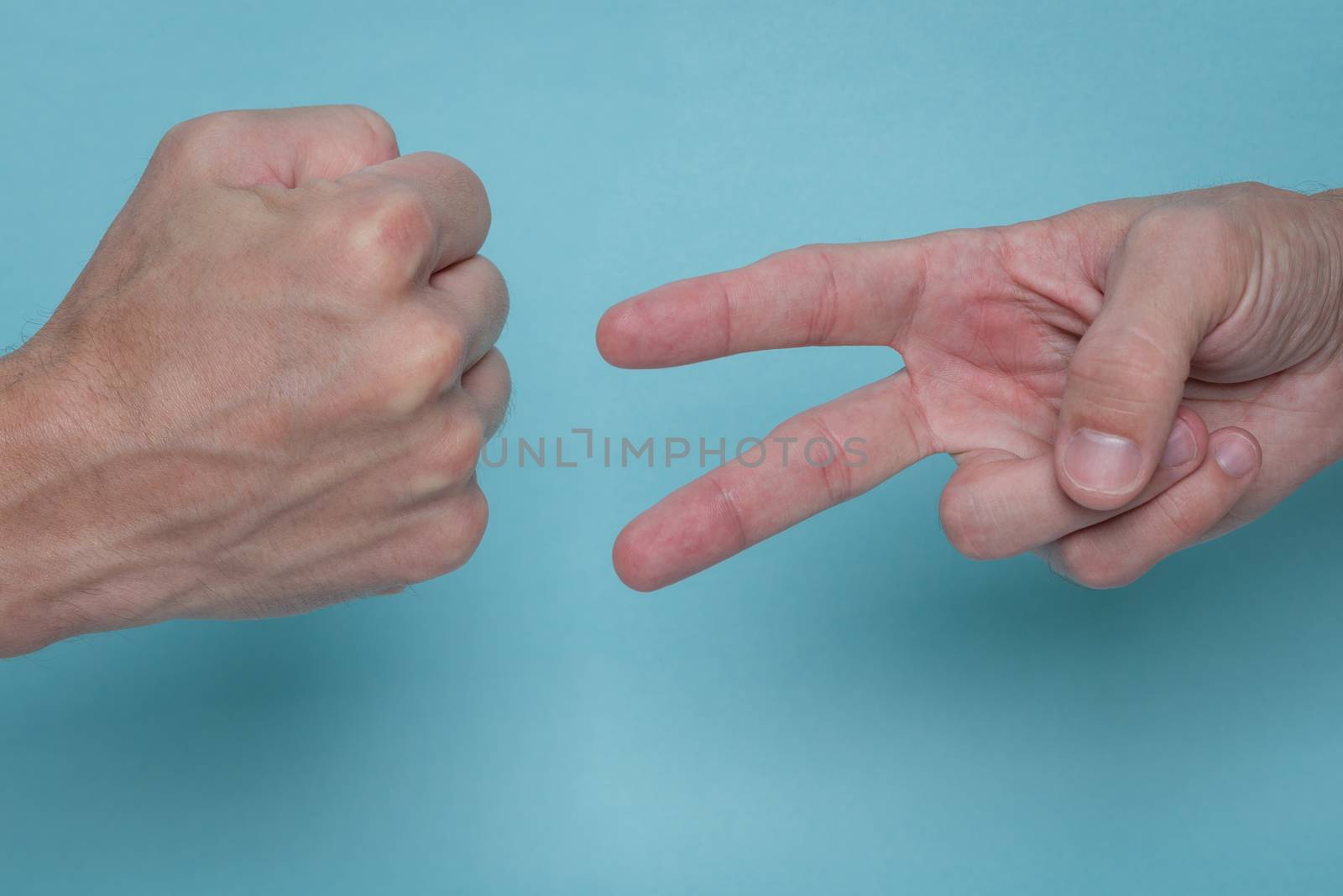 Men's hands playing rock, paper, scissors on a light blue background. One is throwing rock, the other is throwing scissors.