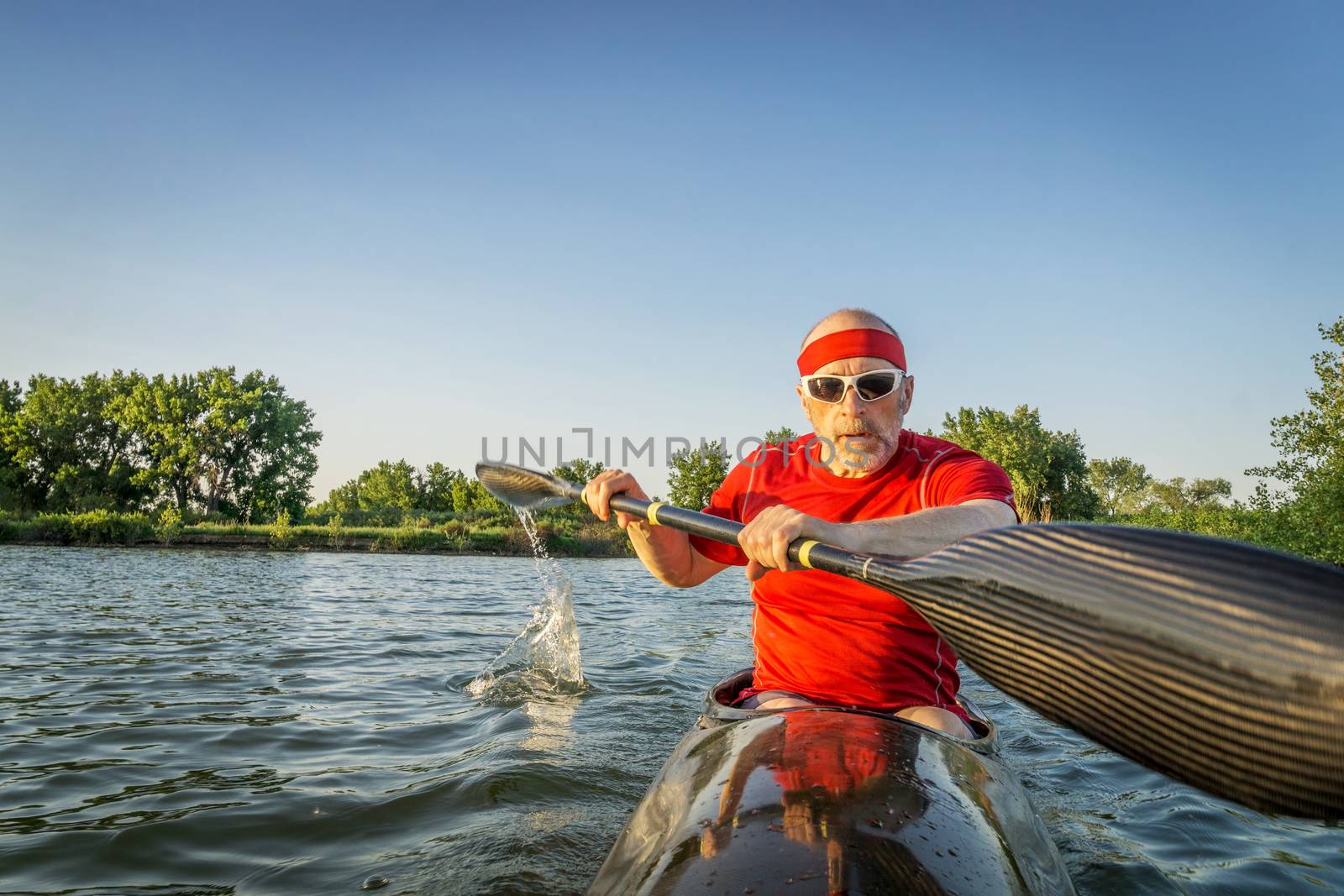 senior male paddler training in a racing sea kayak with a wing paddle on a lake, motion blur of paddle