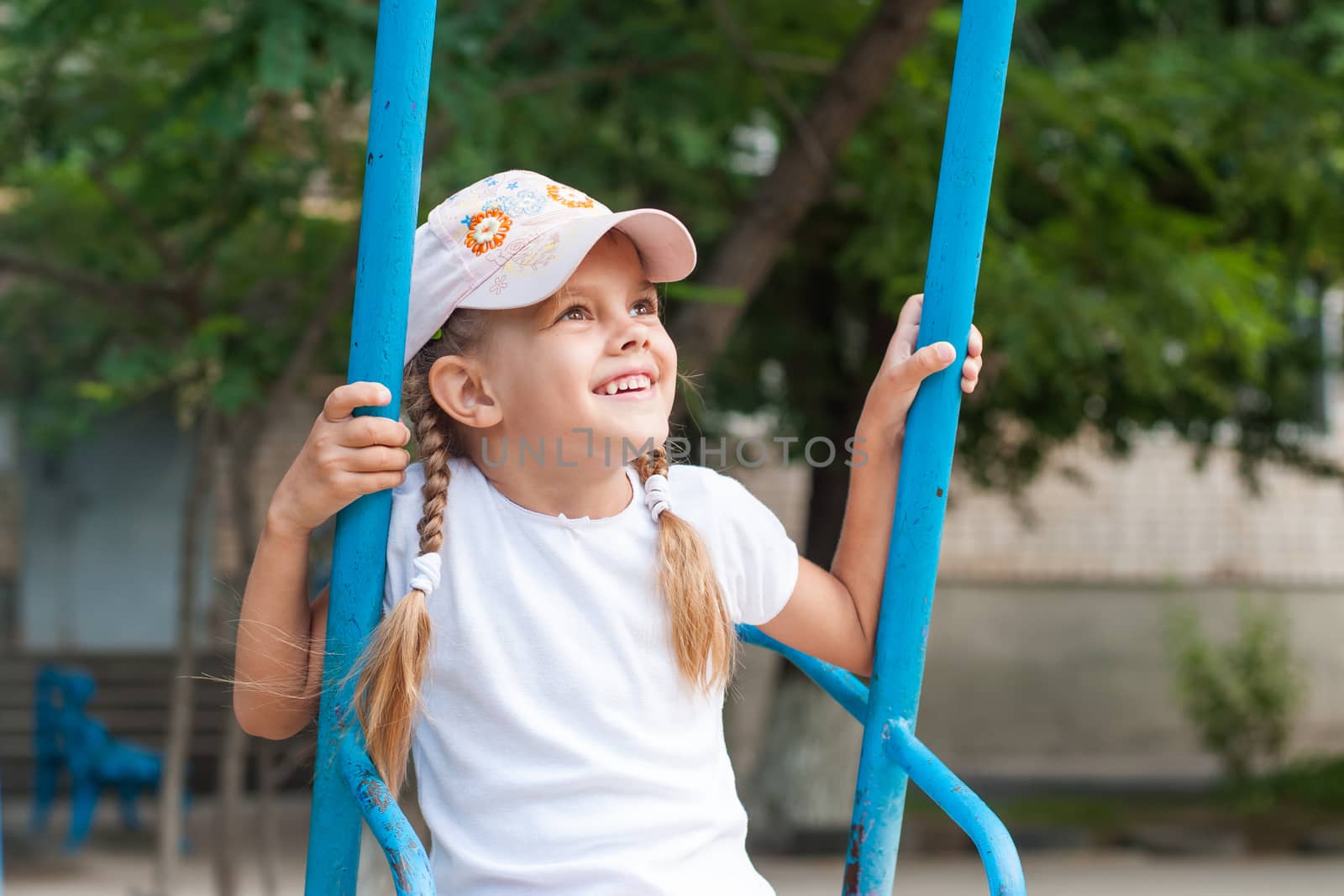 Happy five year old girl riding on a swing at the playground