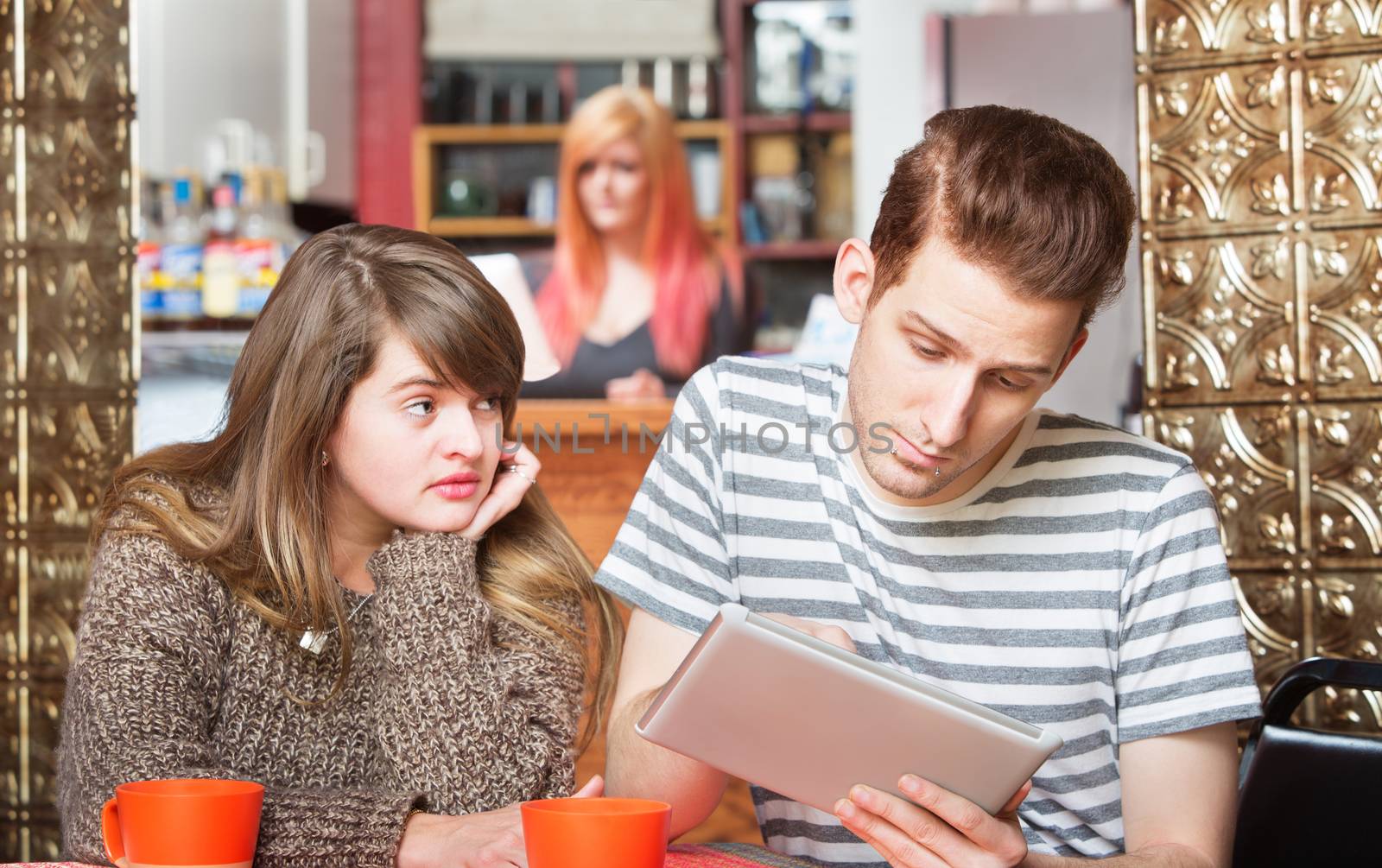 Sad woman looking over at boyfriend using computer tablet