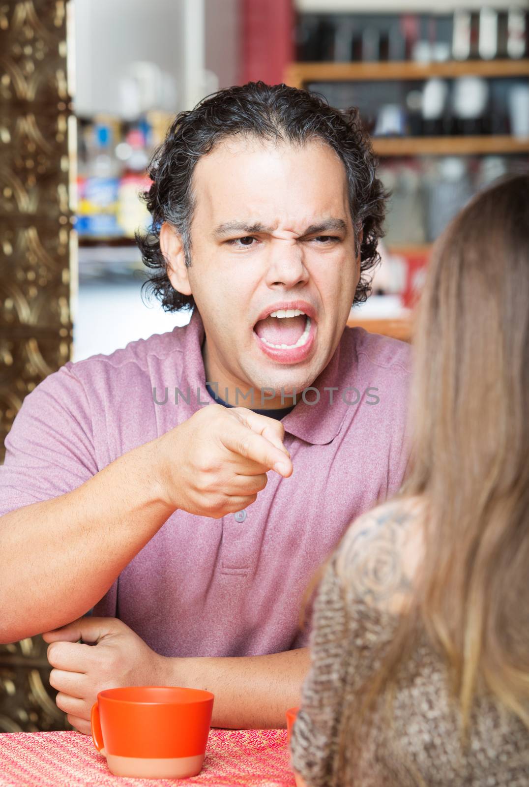 Angry man yelling and pointing at woman in cafe