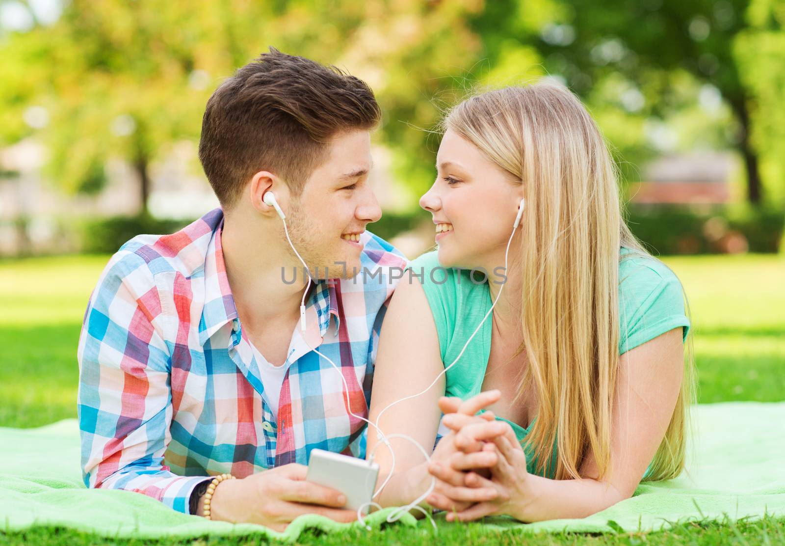 vacation, holidays, technology and friendship concept - smiling couple with smartphone and earphones lying on blanket in park